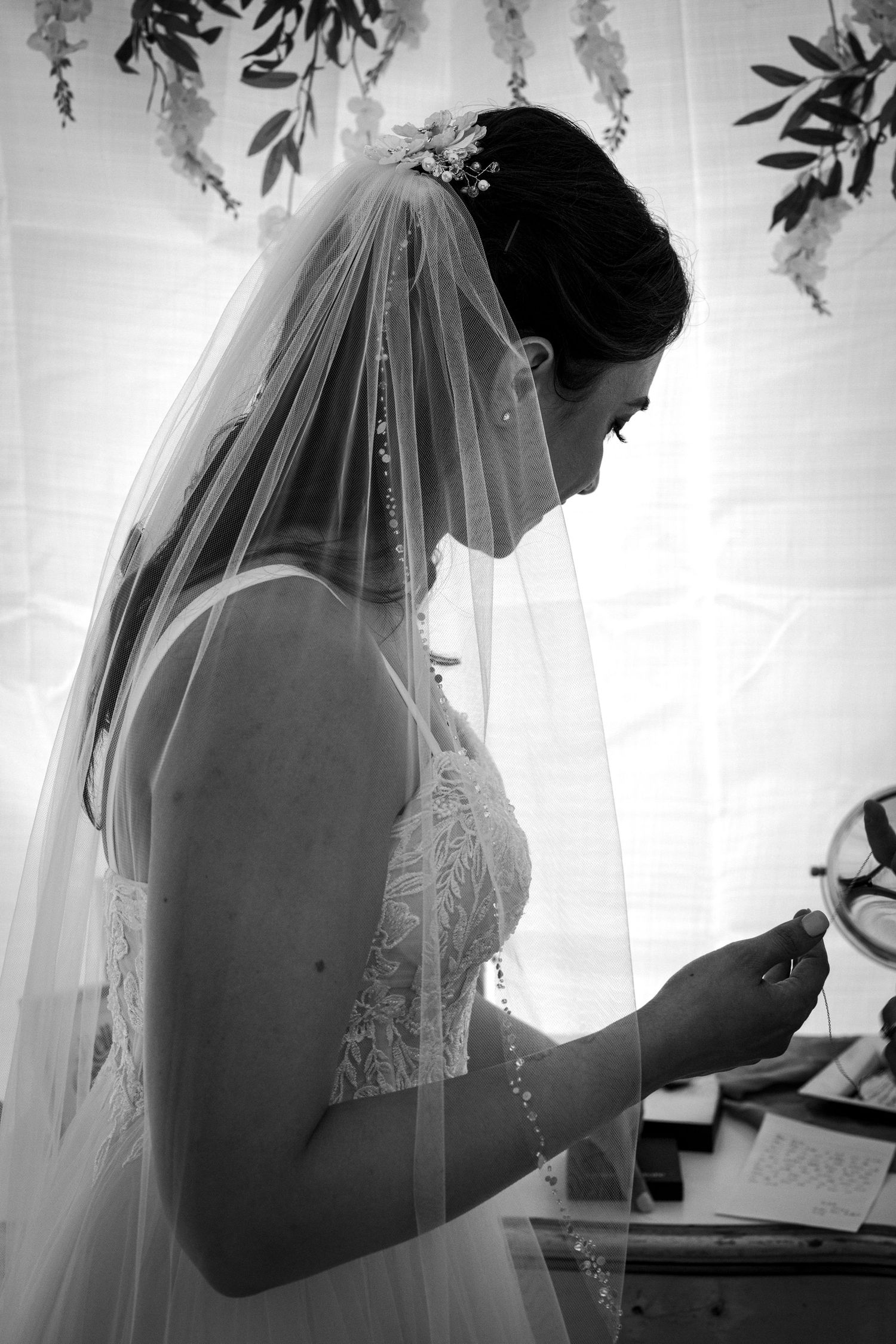 A bride in a delicate lace wedding dress and embellished veil stands in a serene black and white moment.