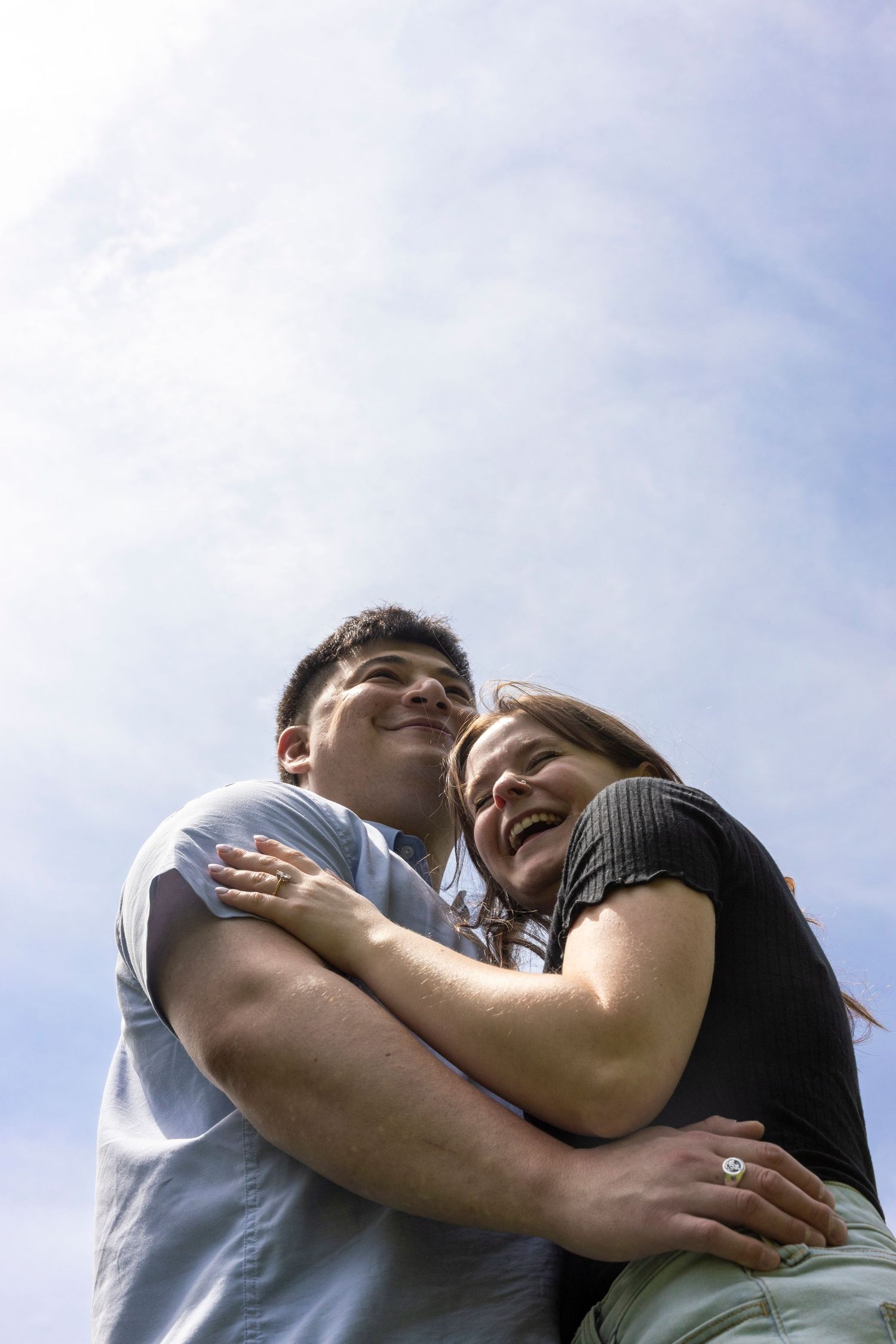 A loving couple embraces while laughing together against a bright blue sky background.