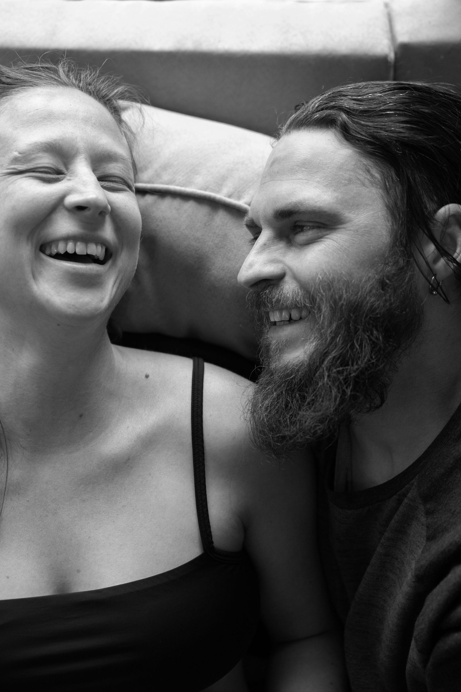 A black and white portrait shows a couple laughing together in an intimate close-up shot.