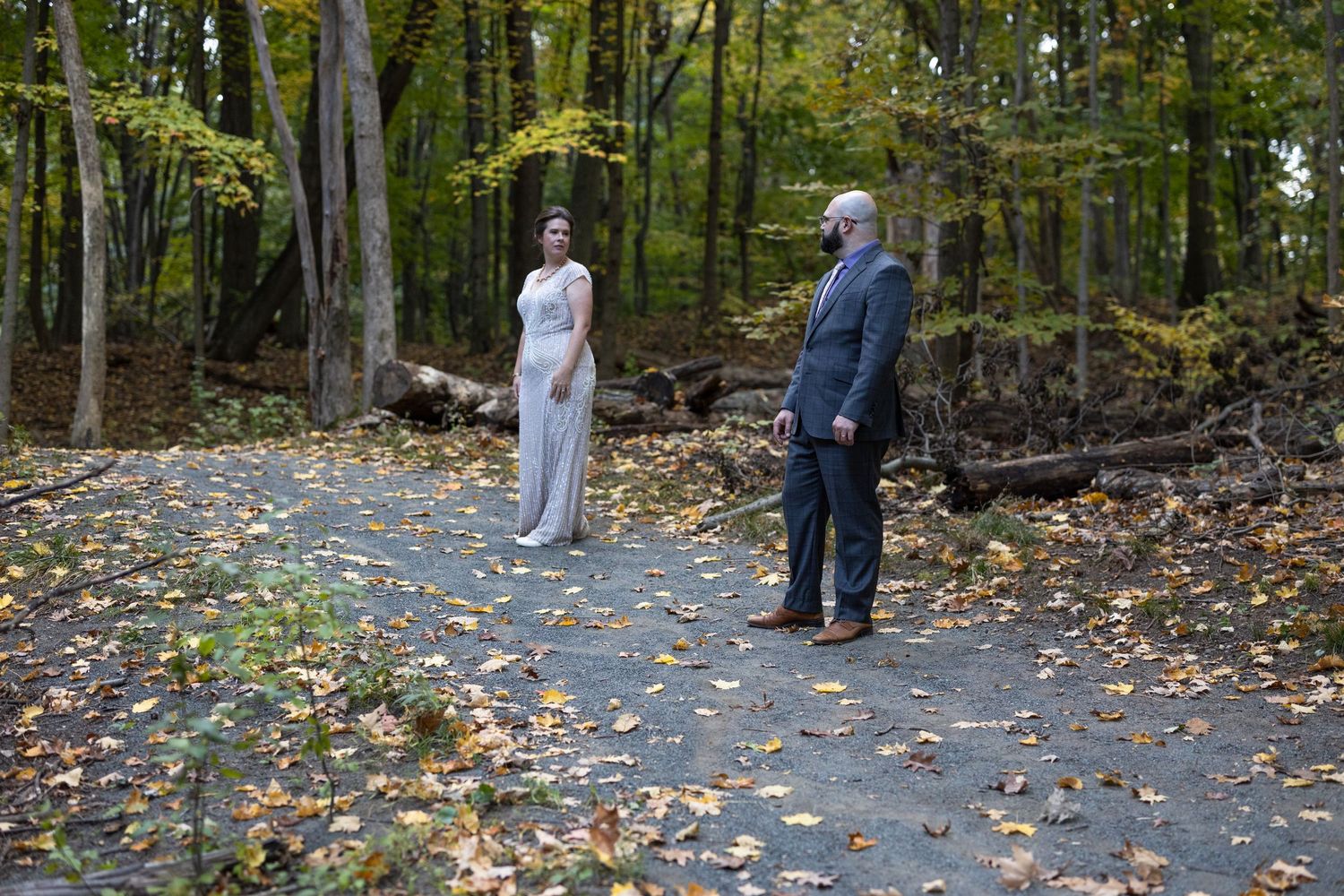 Among autumn leaves and trees, someone walks down a forested path in white clothing and surgical mask.