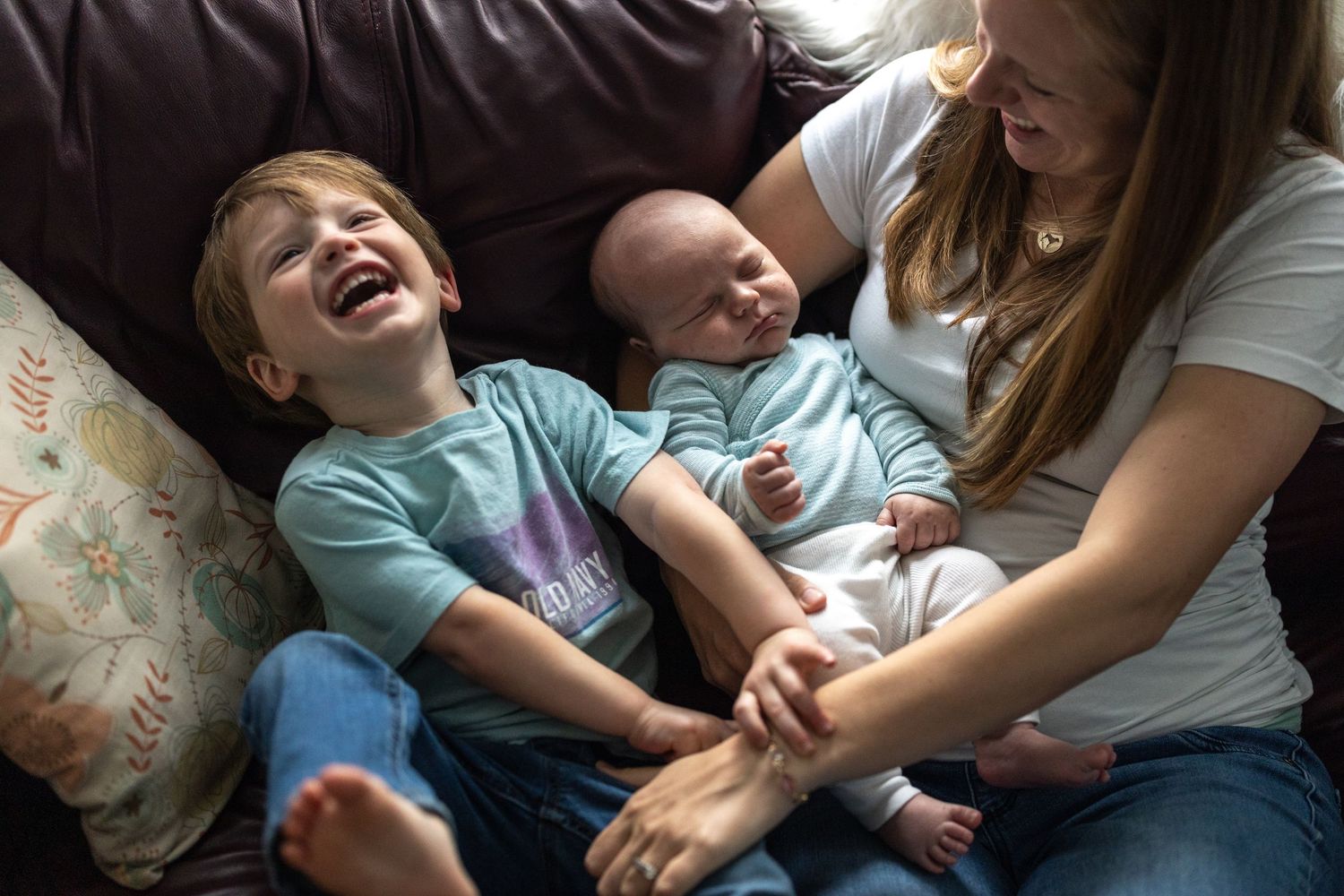 A joyful candid family moment captured on a dark couch, showing playful interaction and laughter.