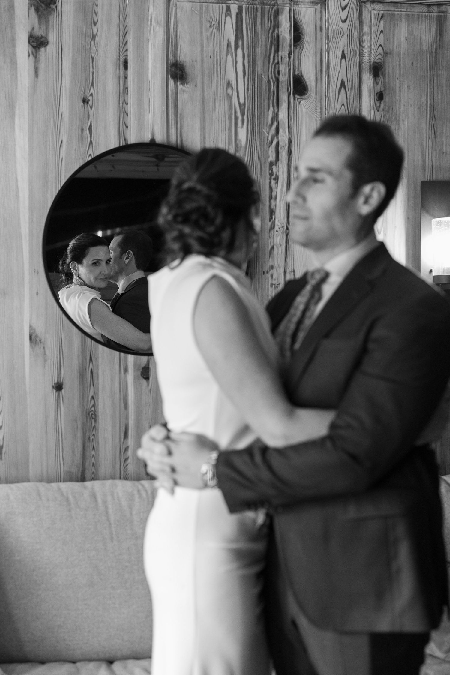 A romantic black and white moment of a couple dancing while their reflection appears in a mirror on a wood-paneled wall.
