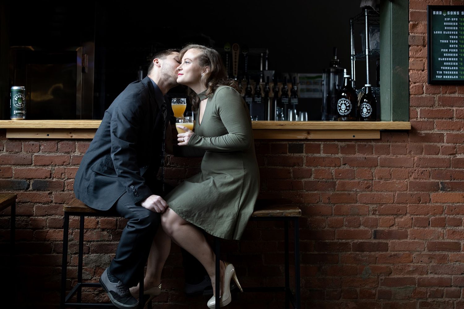 A couple embraces in an intimate moment against a rustic brick wall at a cozy bar setting.