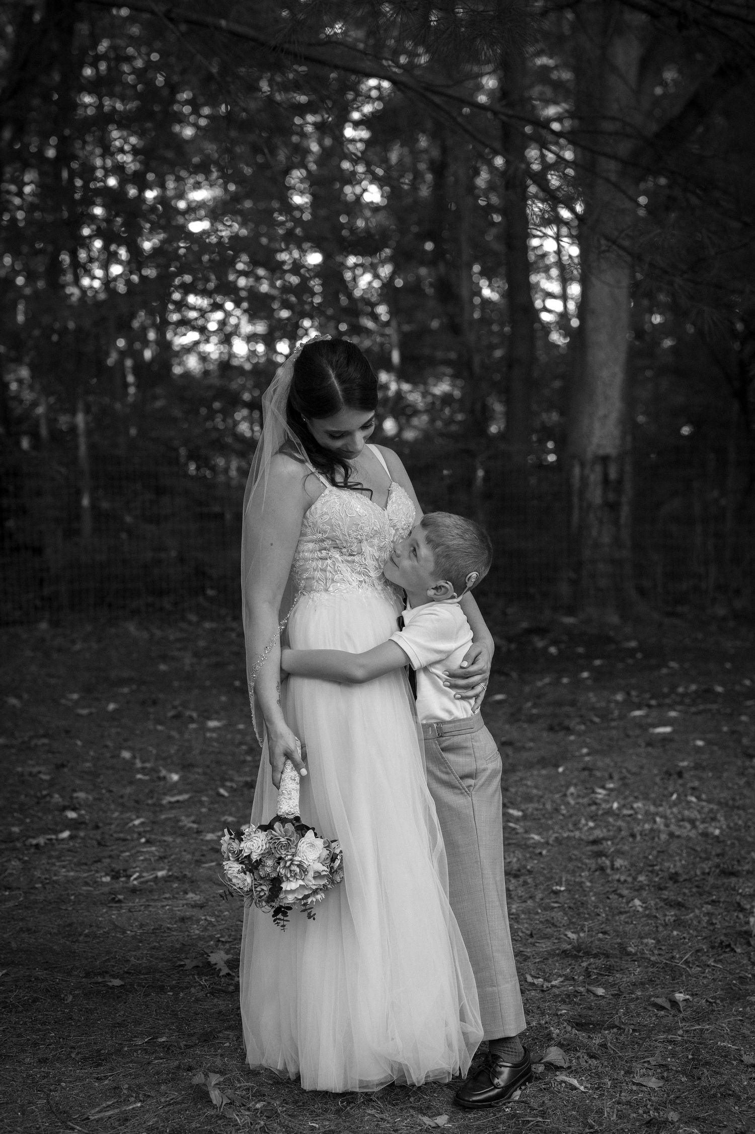 A tender black and white wedding moment captured in a wooded setting with a bride holding a floral bouquet.