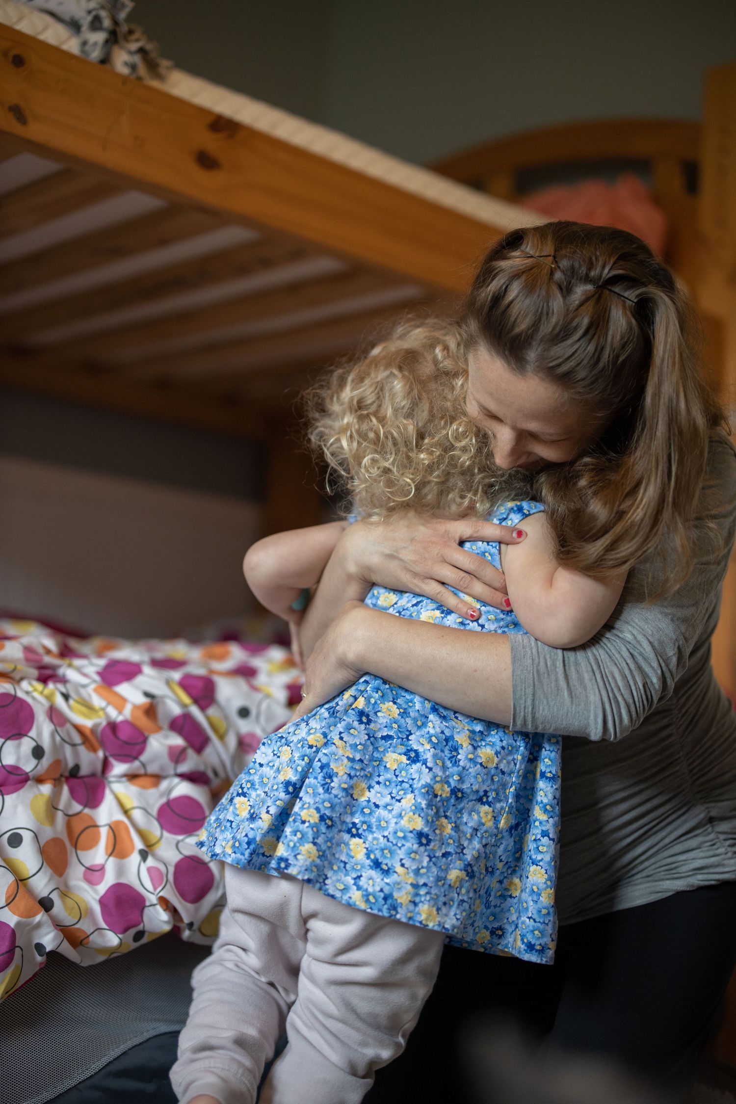 A tender embrace between an adult in gray and a small child wearing a blue floral dress on a colorful bed.