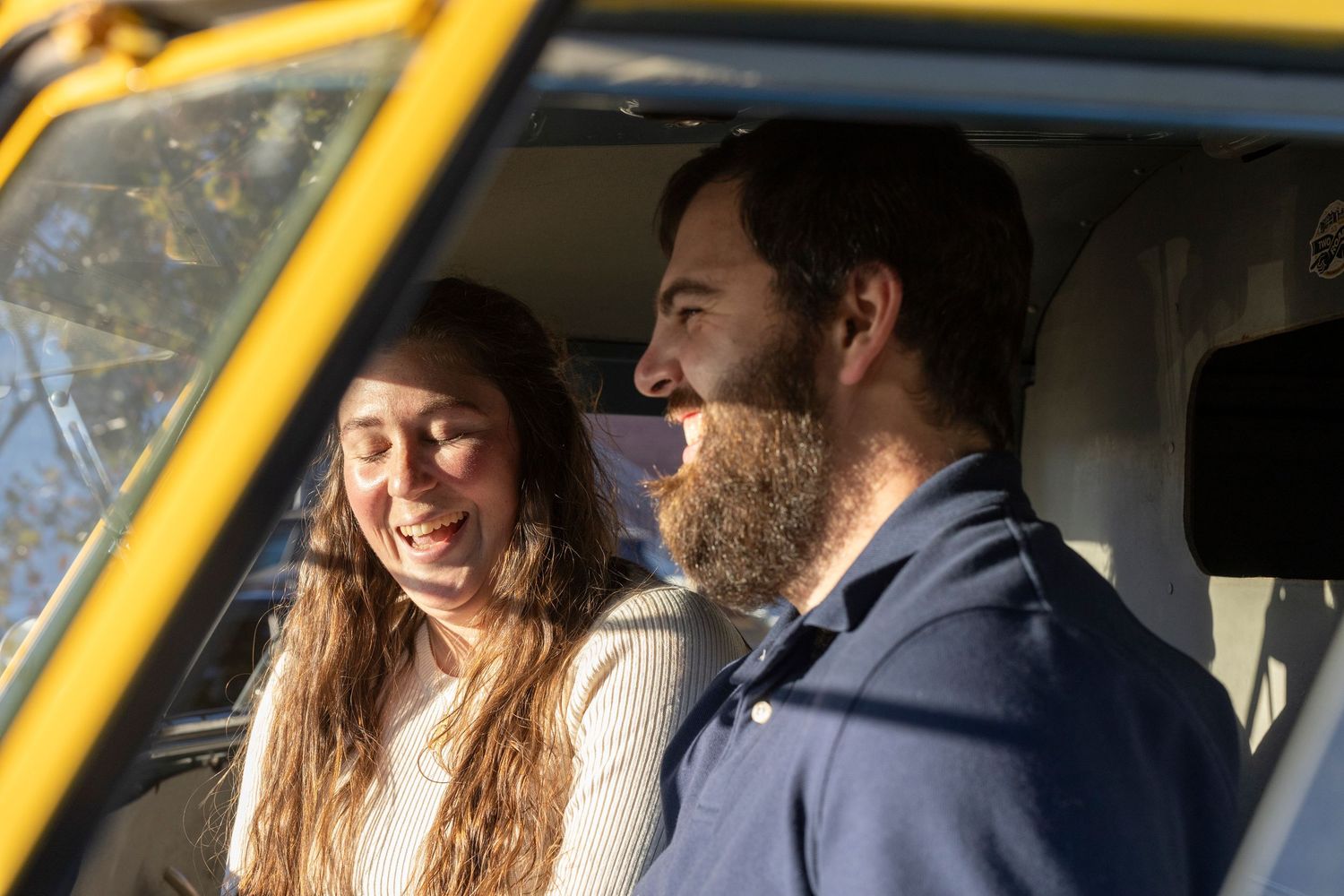 Two people laughing together while sitting in a yellow vehicle in natural lighting.