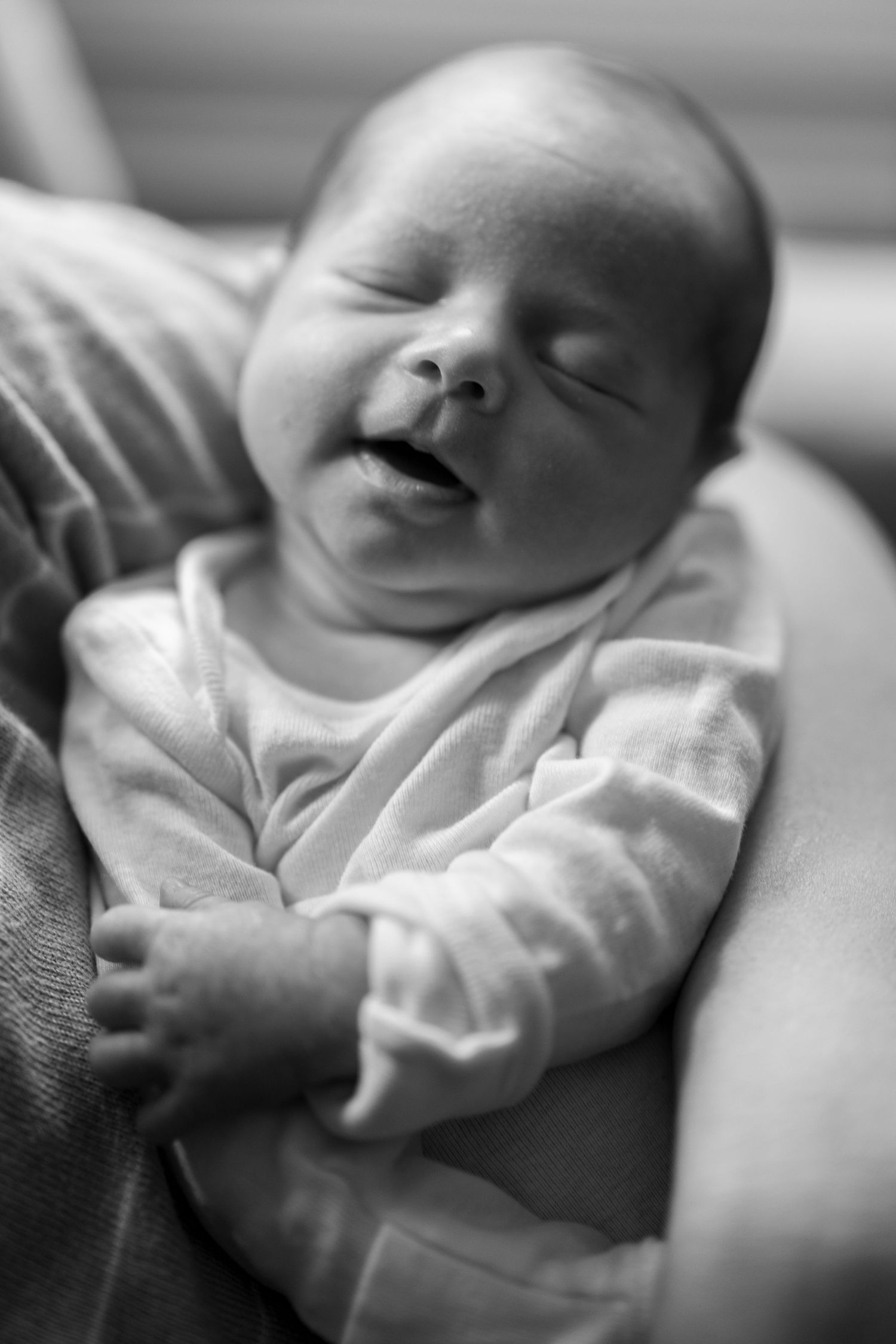 A peaceful sleeping baby in a white onesie smiles contentedly in black and white photograph.