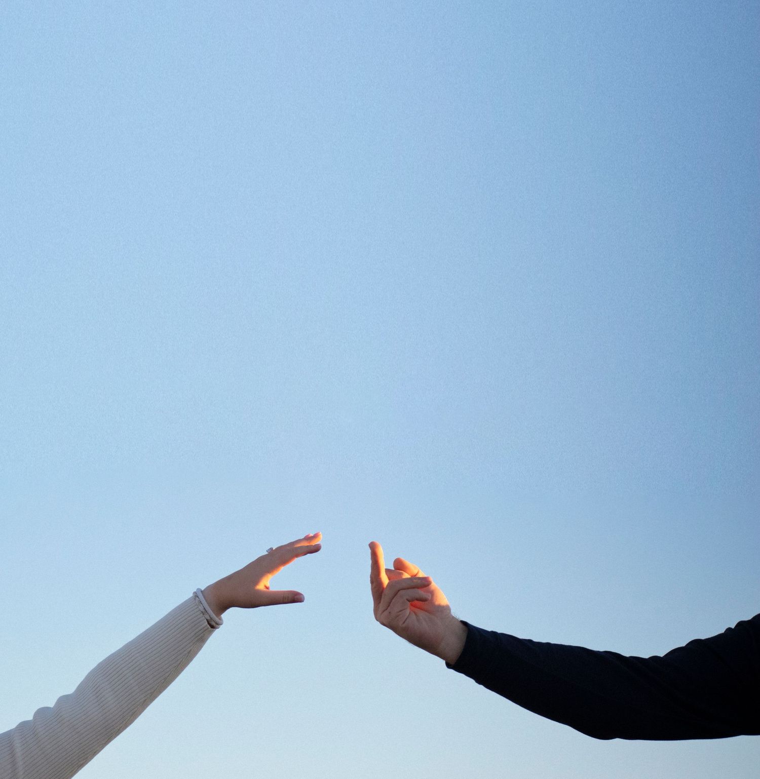 Two hands reaching up to touch against a blue sky background, painted in contrasting light and dark sleeves.