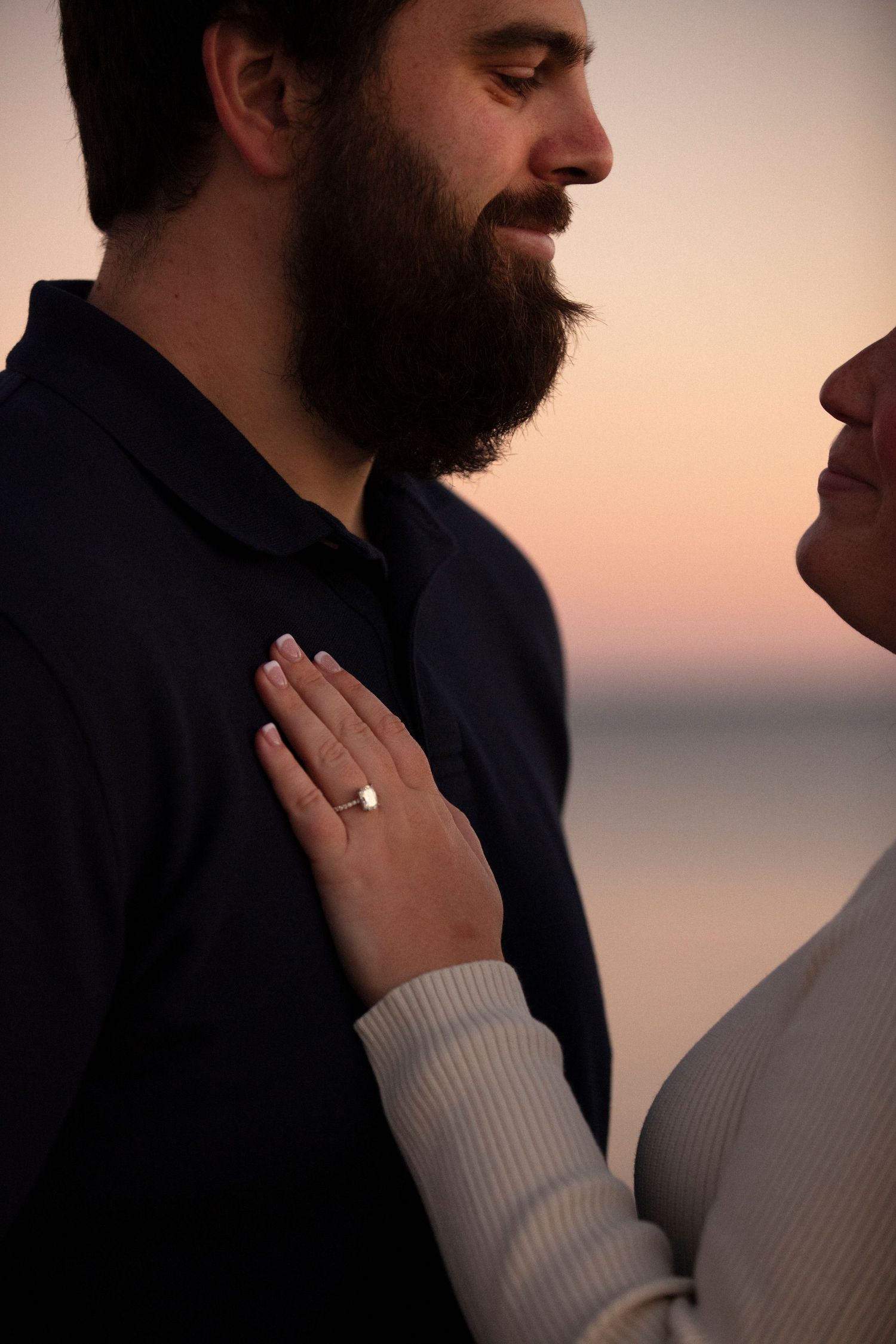 Close-up portrait of an intimate moment between a couple at sunset showing an engagement ring and warm lighting.