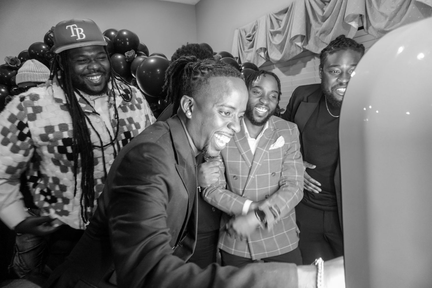 A group of people laugh together in a black and white photo showing joyful expressions and camaraderie.