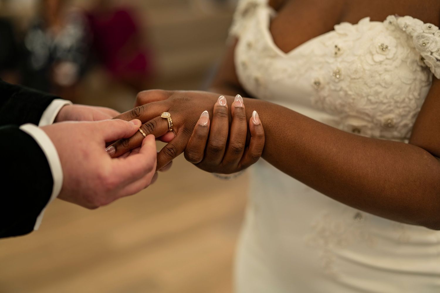 Close-up shot of wedding ring exchange during ceremony with formal attire.