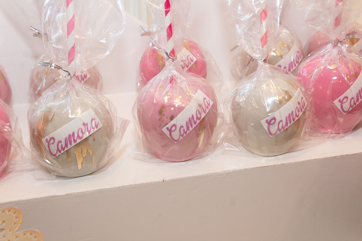 Pink and white candy apples wrapped in clear cellophane packaging sit lined up on a white display shelf.