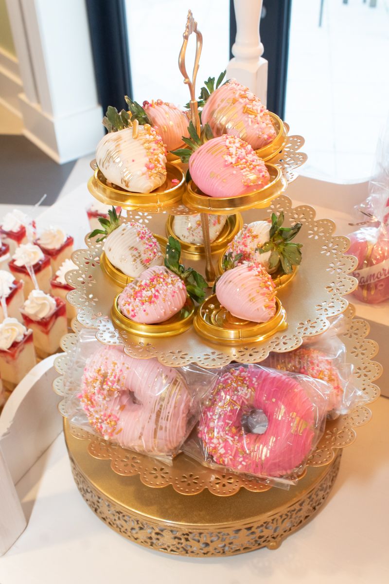Elegant tiered dessert stand with pink donuts and treats on gold scalloped plates.