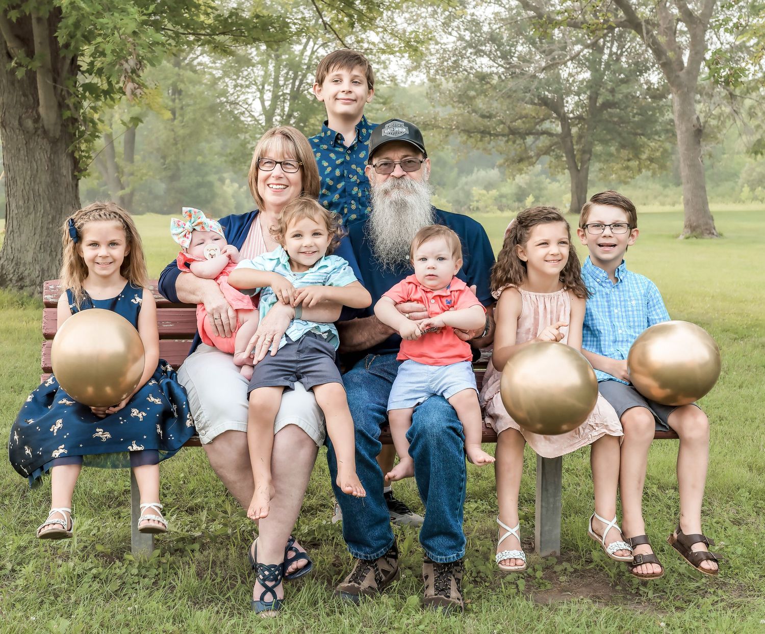 Large family group portrait outdoors with multiple children and adults sitting together on grass.