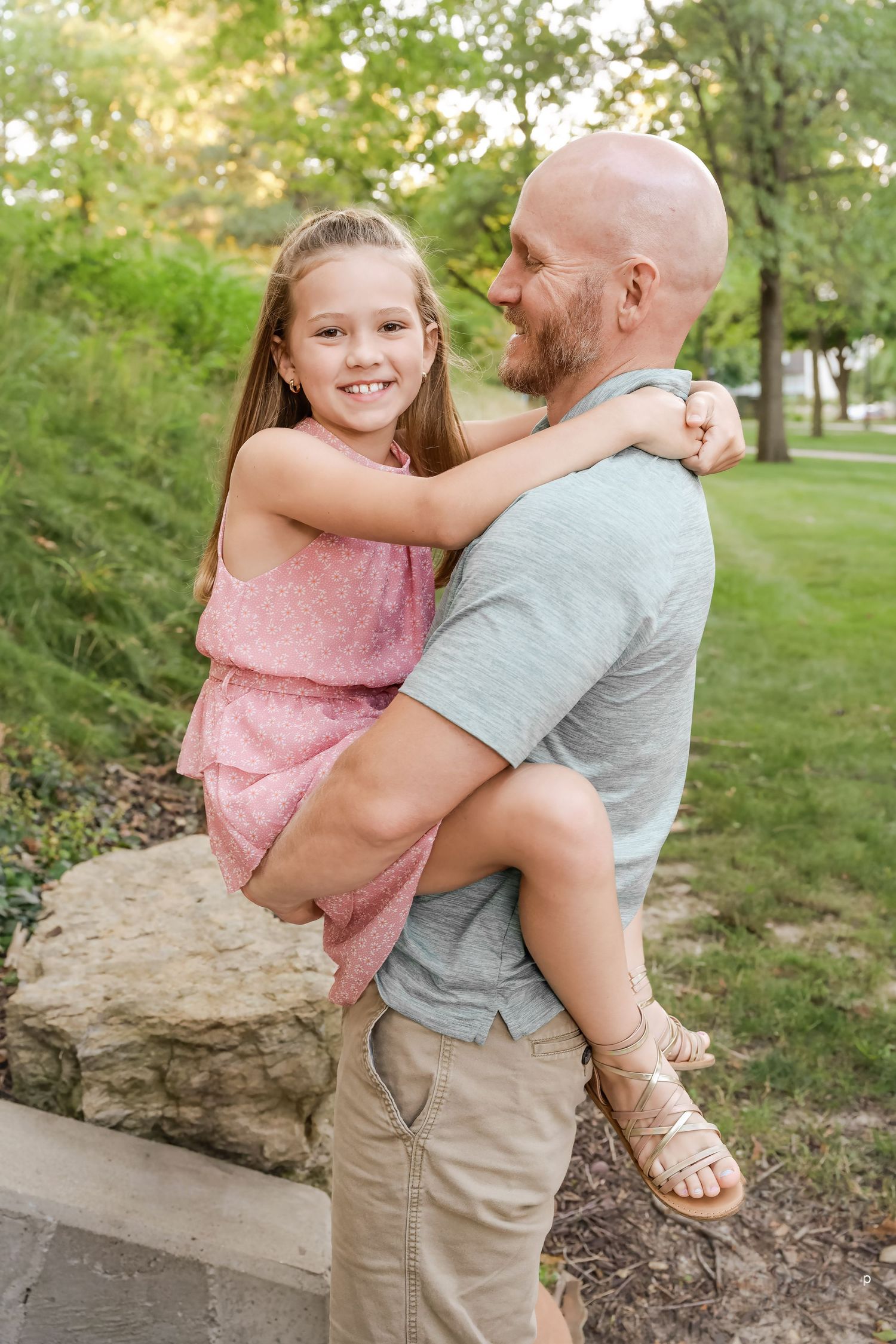 Father and daughter share a joyful embrace while standing in a park on a sunny afternoon.