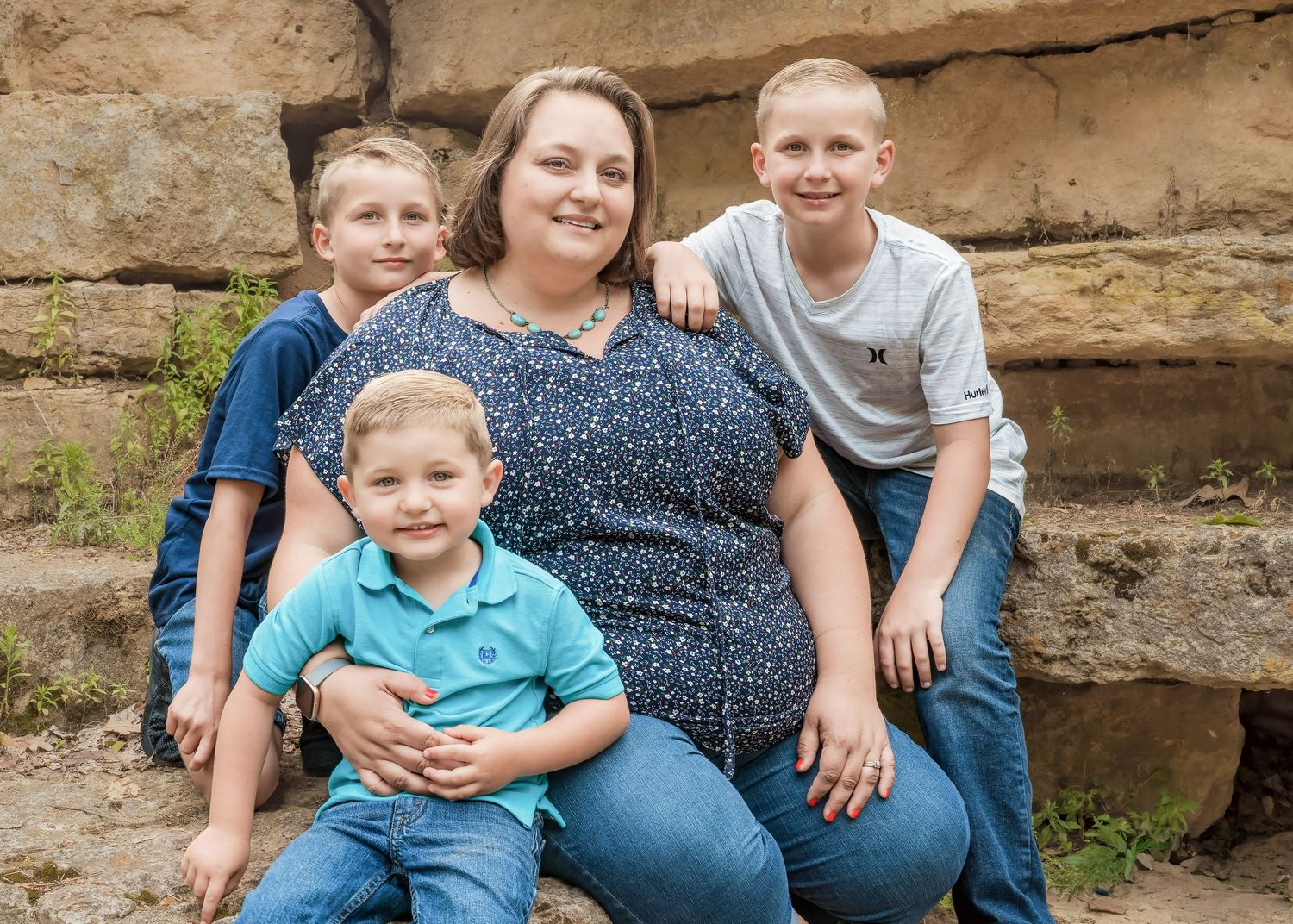 Family of four posing together against rocky wall background outdoors.