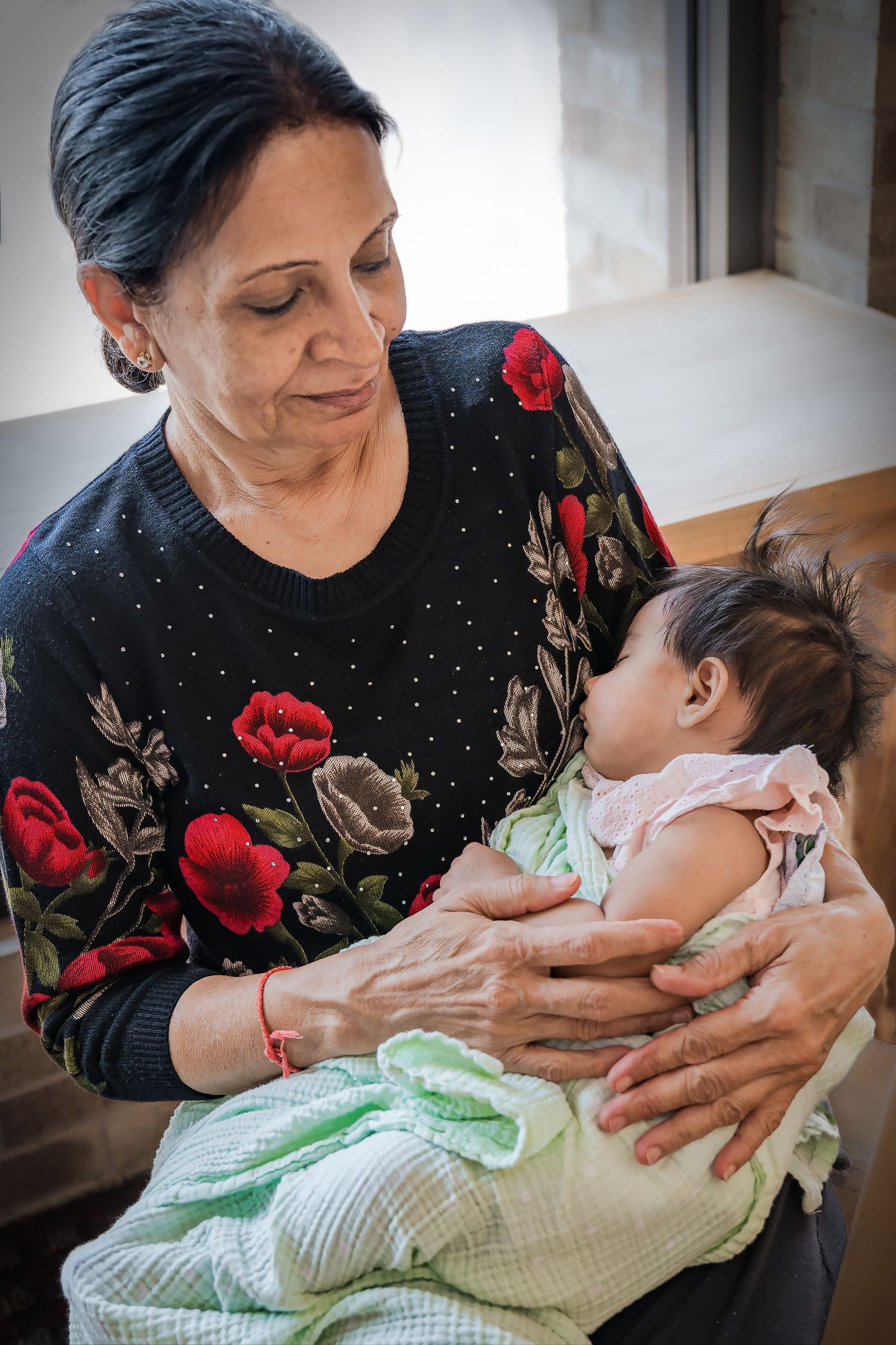 Woman in floral sweater holding and caring for small baby wrapped in mint green blanket.