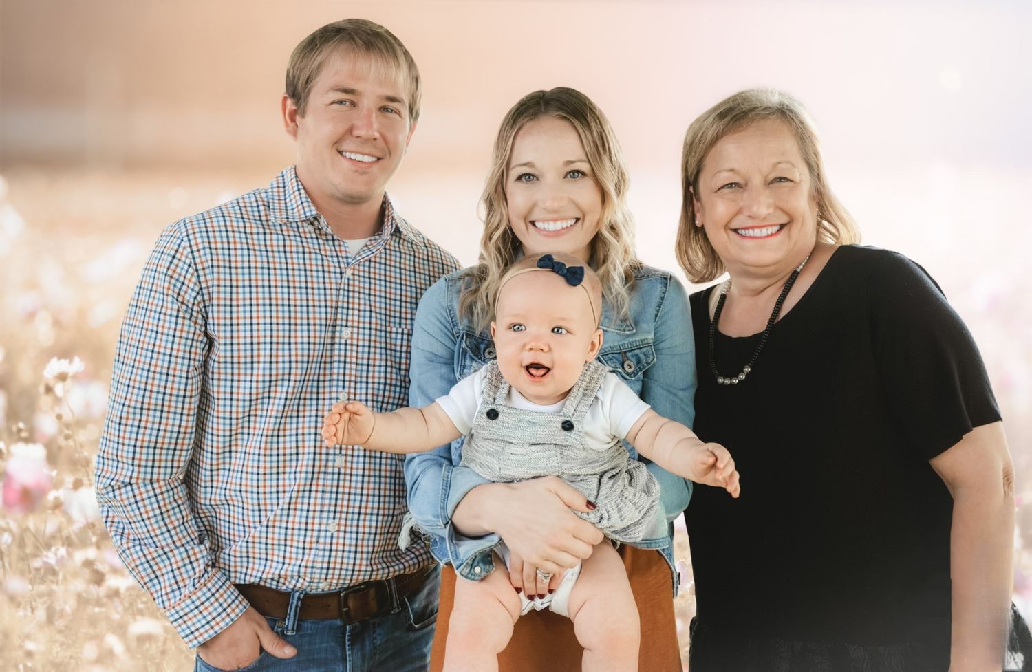 Family photo featuring three adults and a joyful baby wearing light blue against a soft neutral background.