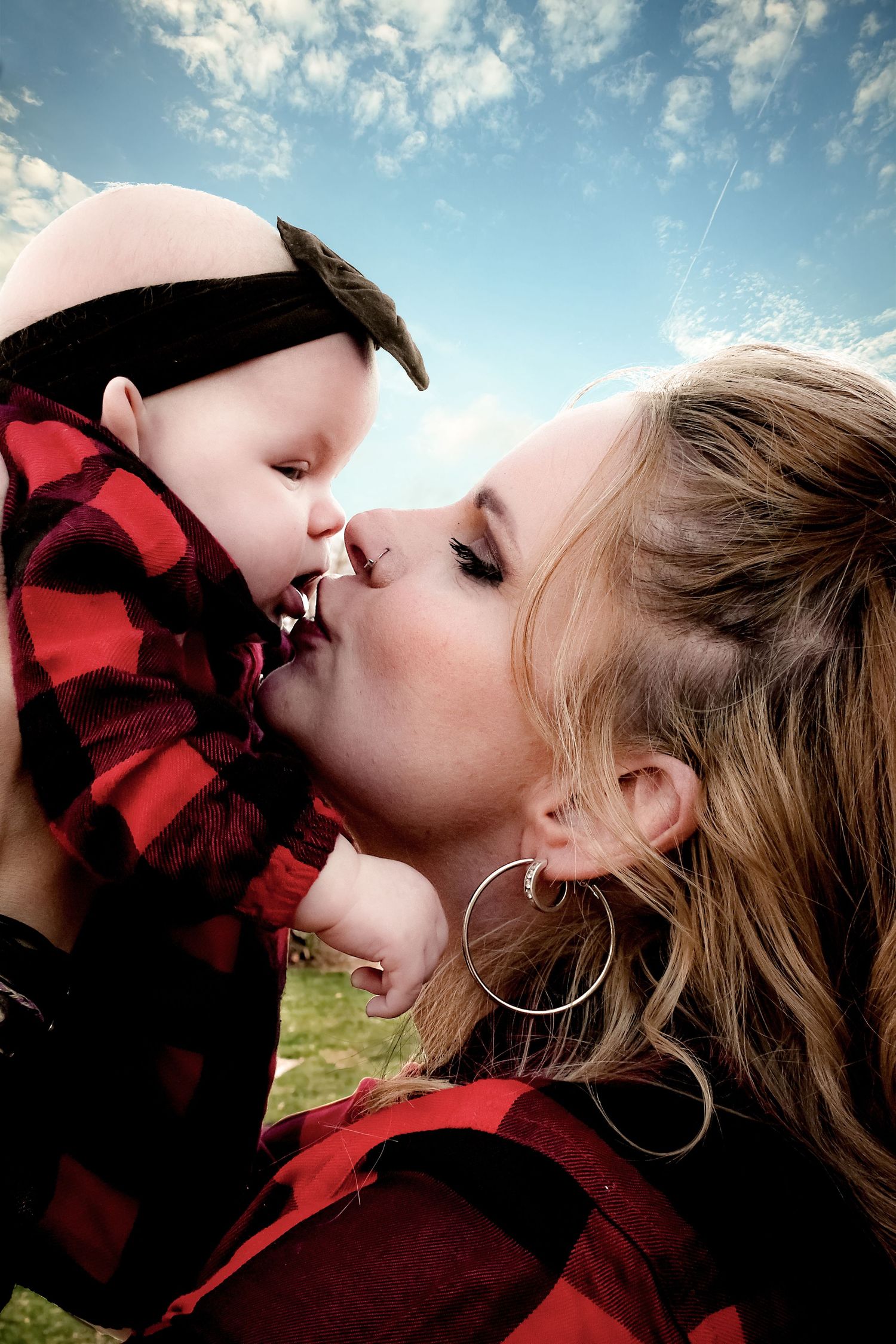 An intimate moment captured against a blue sky background with matching red buffalo plaid clothing.