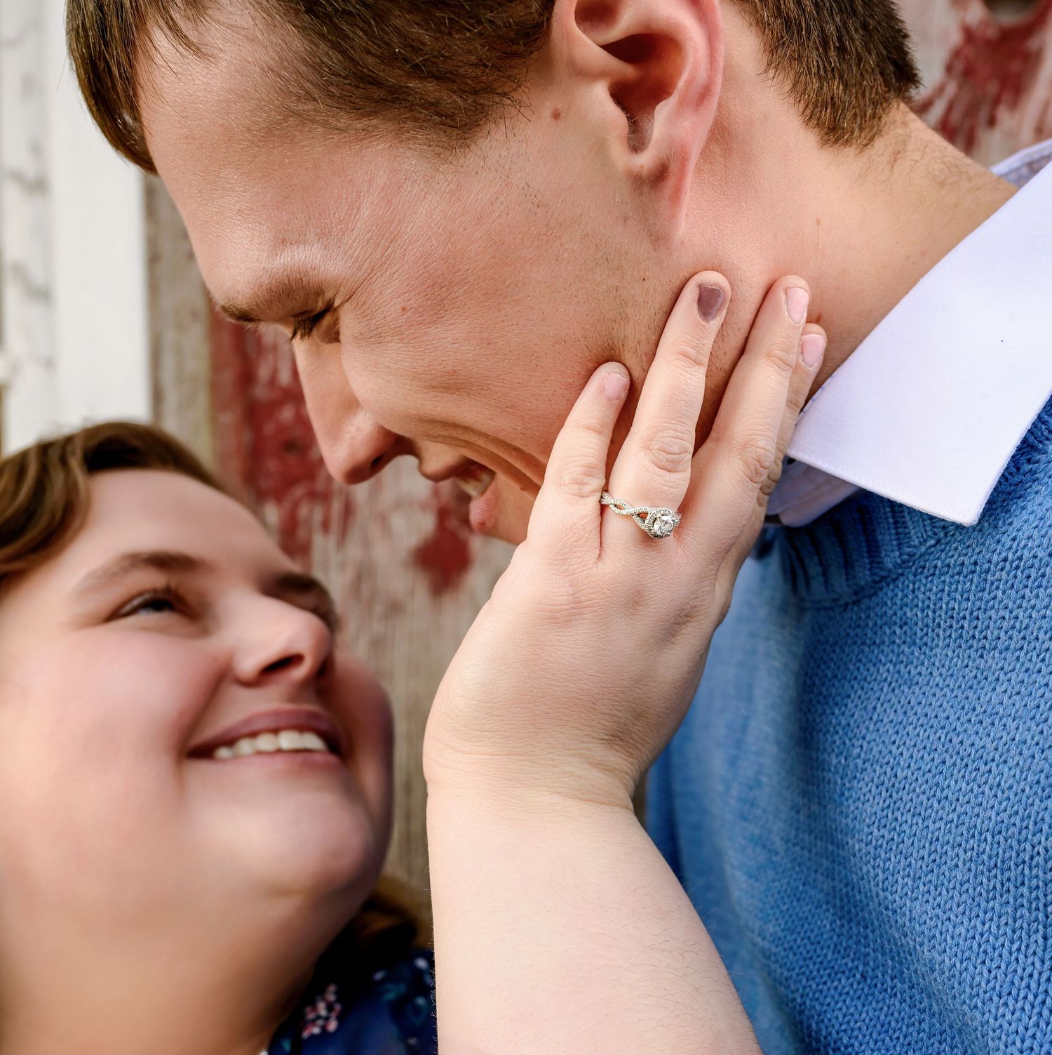 A couple shares an intimate moment as she touches his face, showing off an engagement ring on her hand.