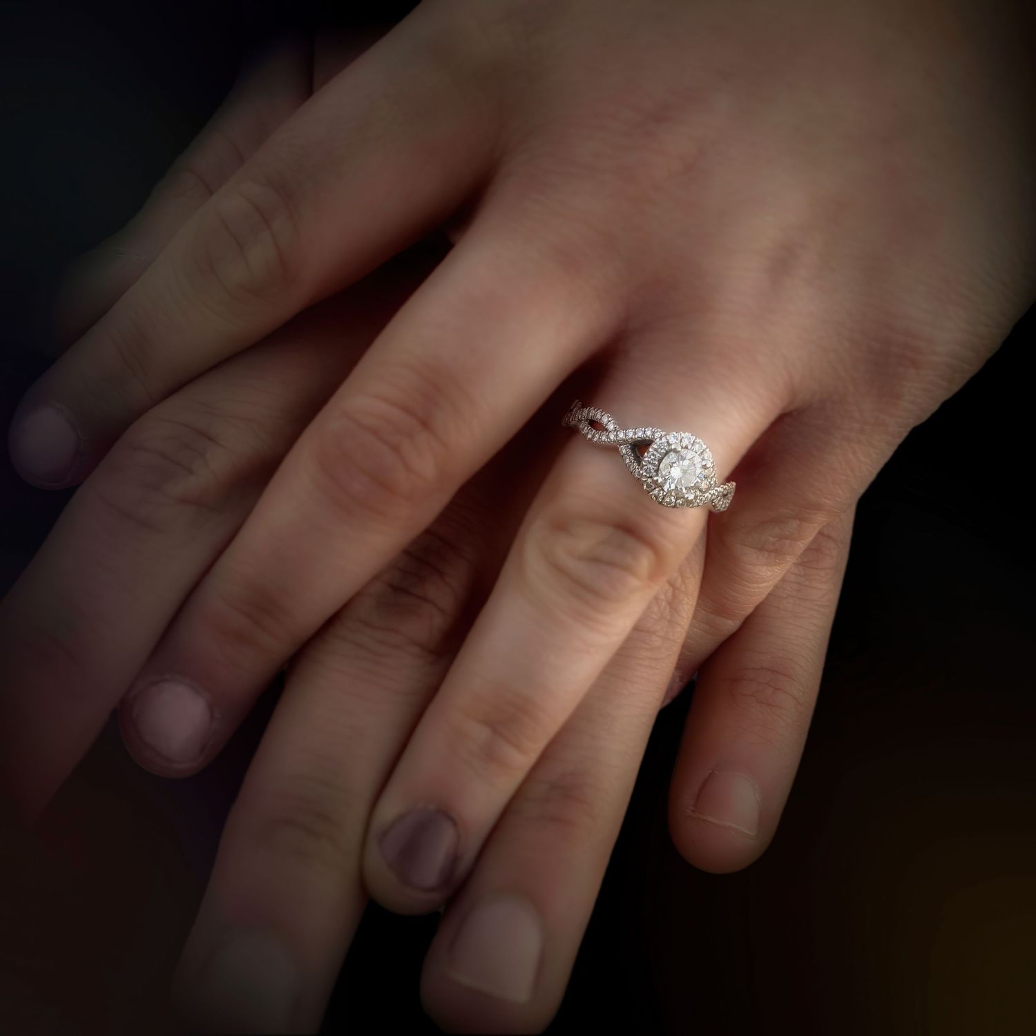A sparkling diamond engagement ring catches the light while being worn on a person's slender hand.