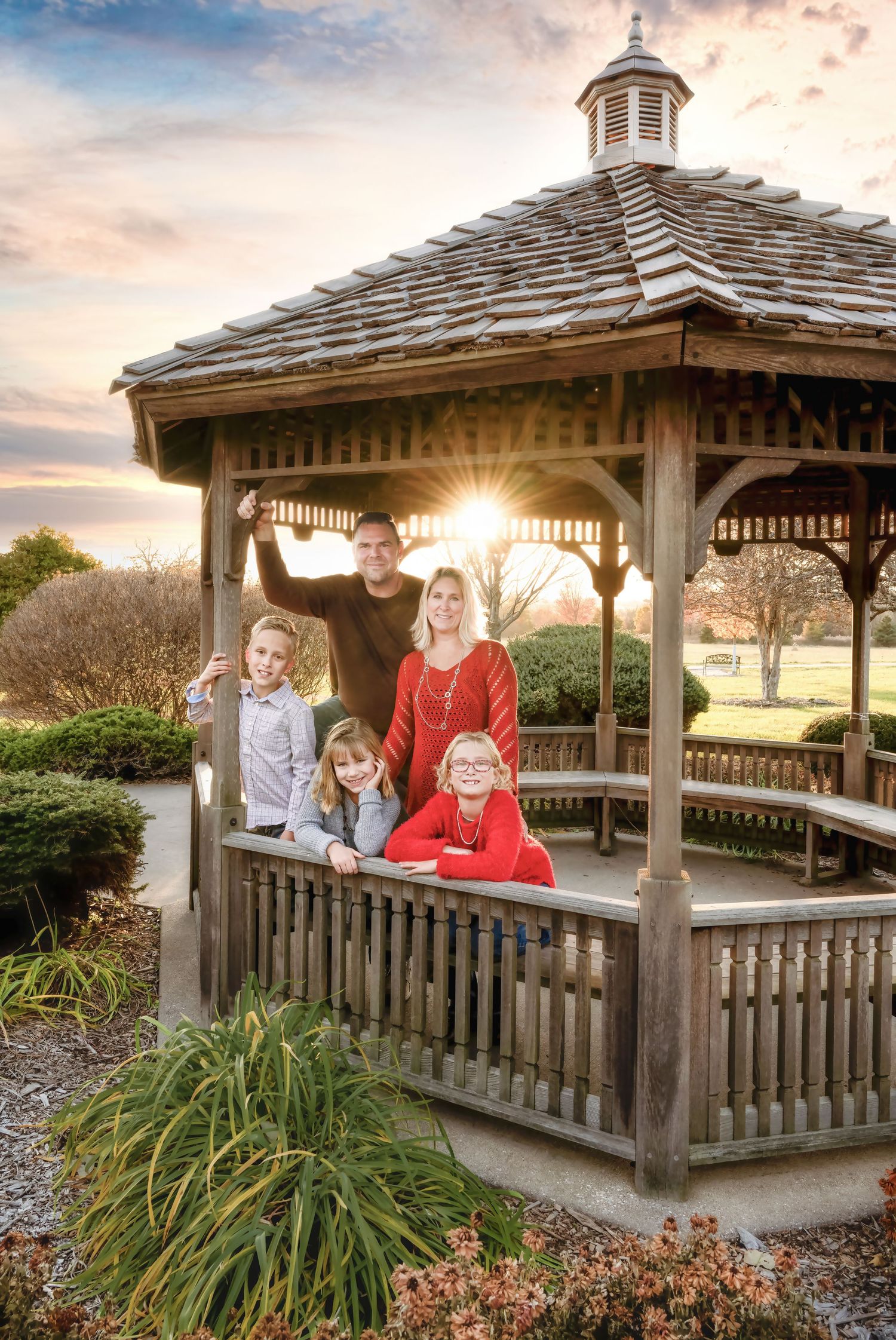 Wooden gazebo in a garden setting at sunset with ornamental grasses and landscaping in the foreground.