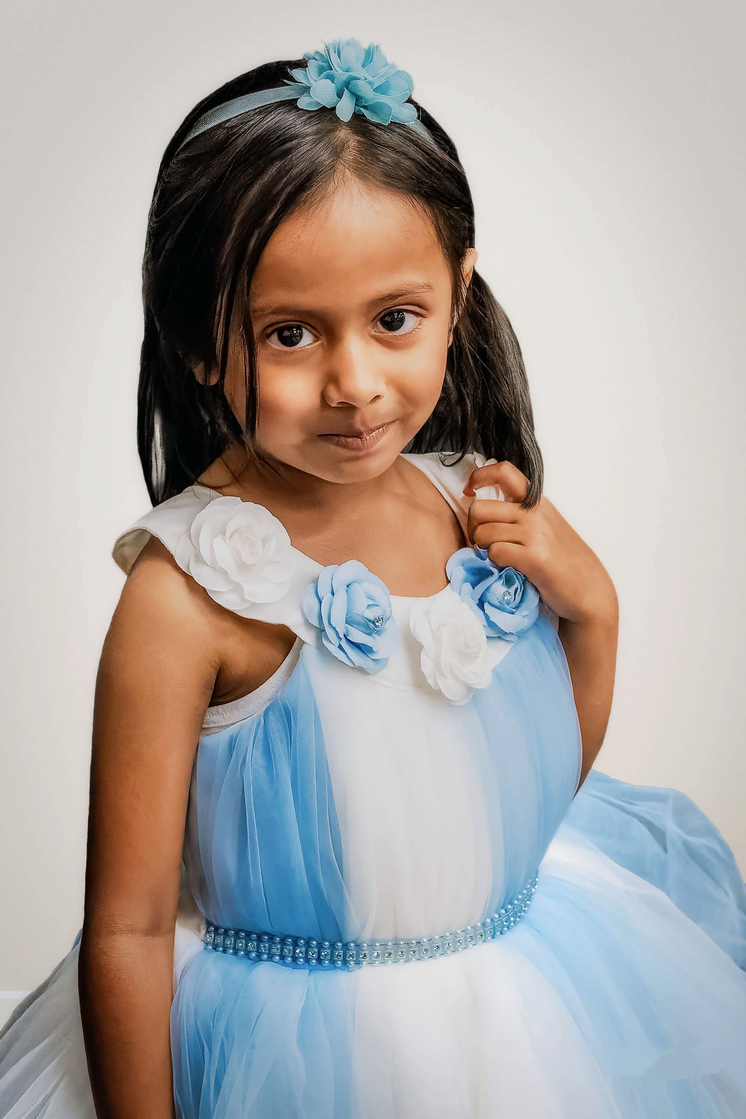 Young girl wearing blue and white tulle dress with floral accents and sparkly belt poses for portrait.