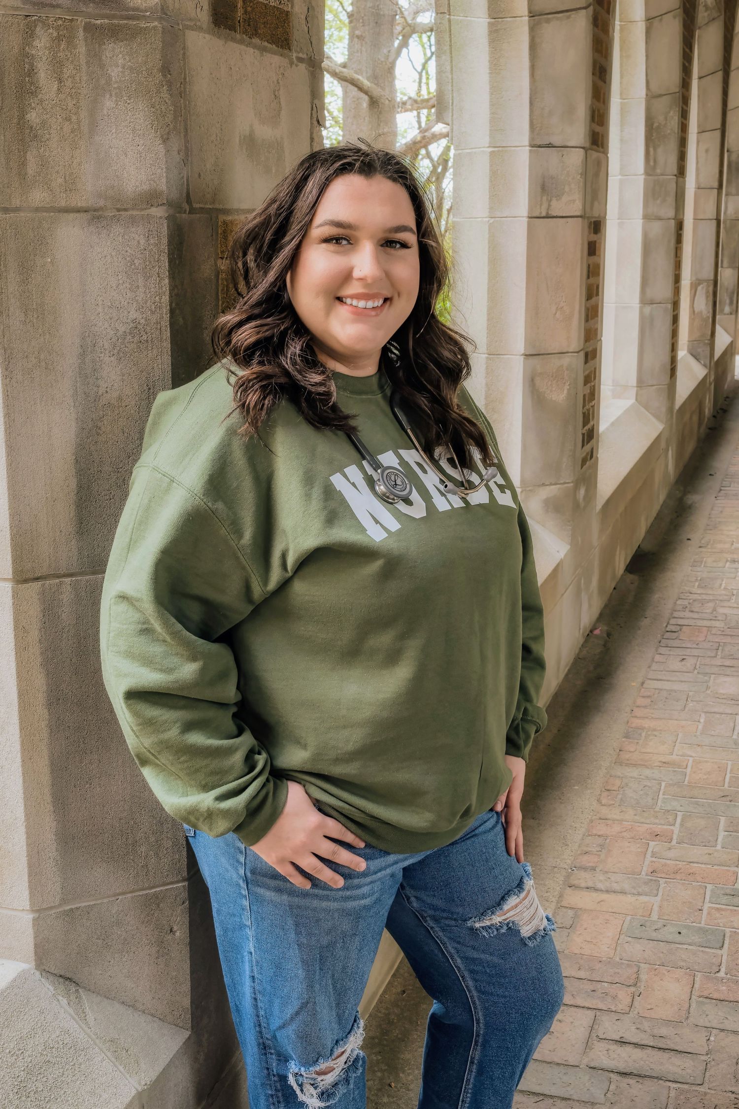 A casual portrait in a green sweatshirt and ripped jeans standing in an ornate stone archway.