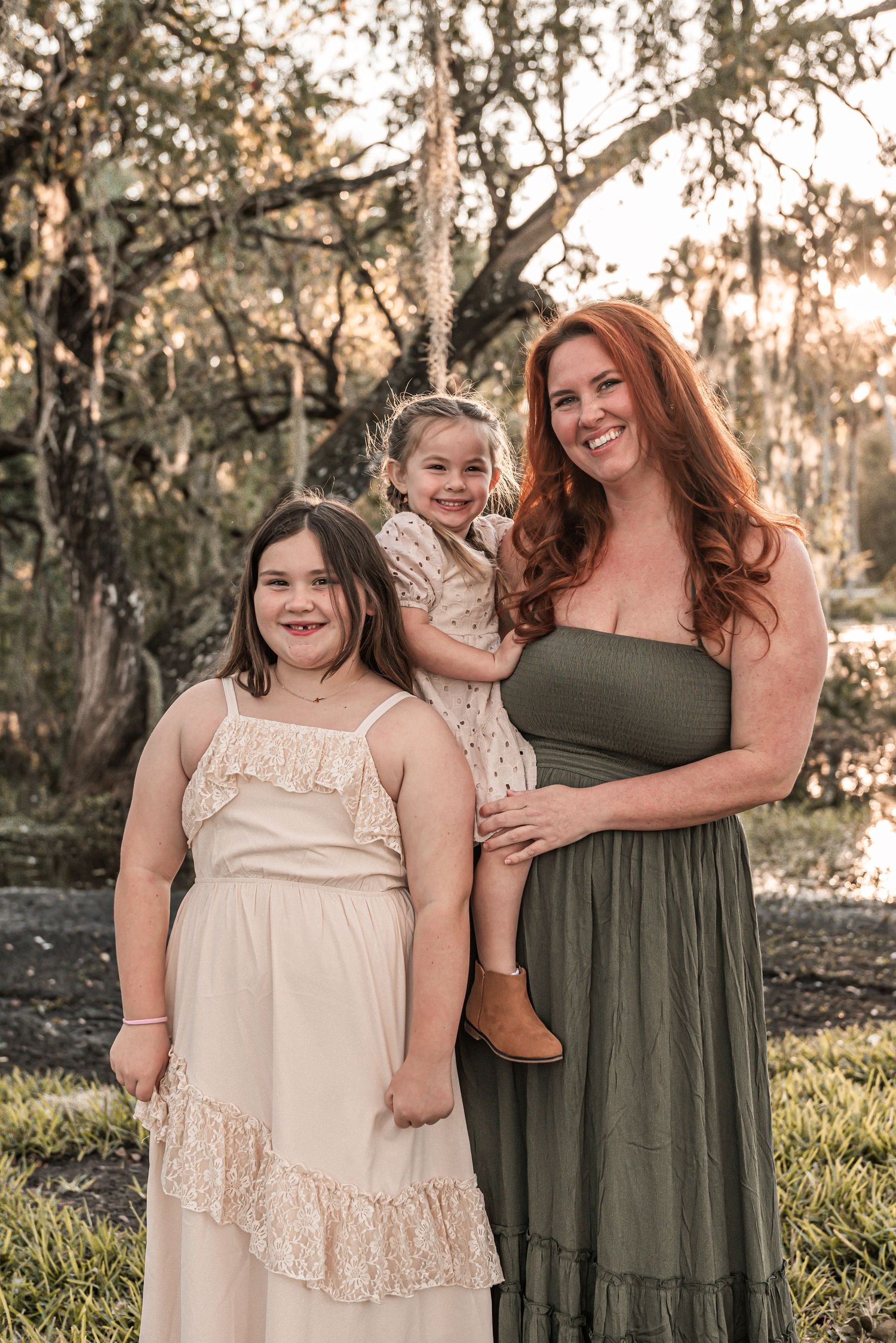Portrait of a family in coordinating dresses standing together outdoors at sunset with trees in the background.
