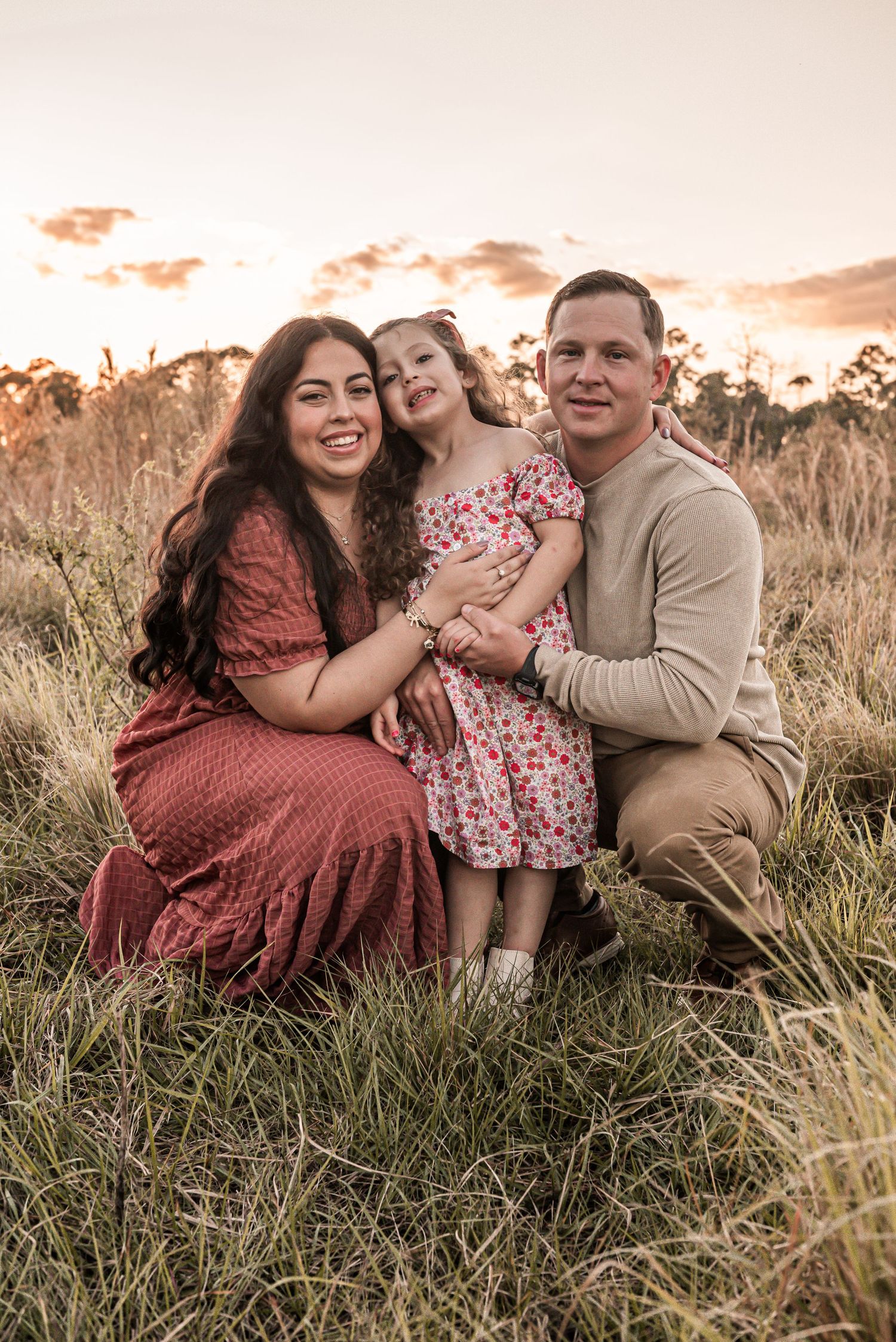 A family portrait at sunset in a golden field with grass, featuring warm earth-toned clothing and a dreamy atmosphere.