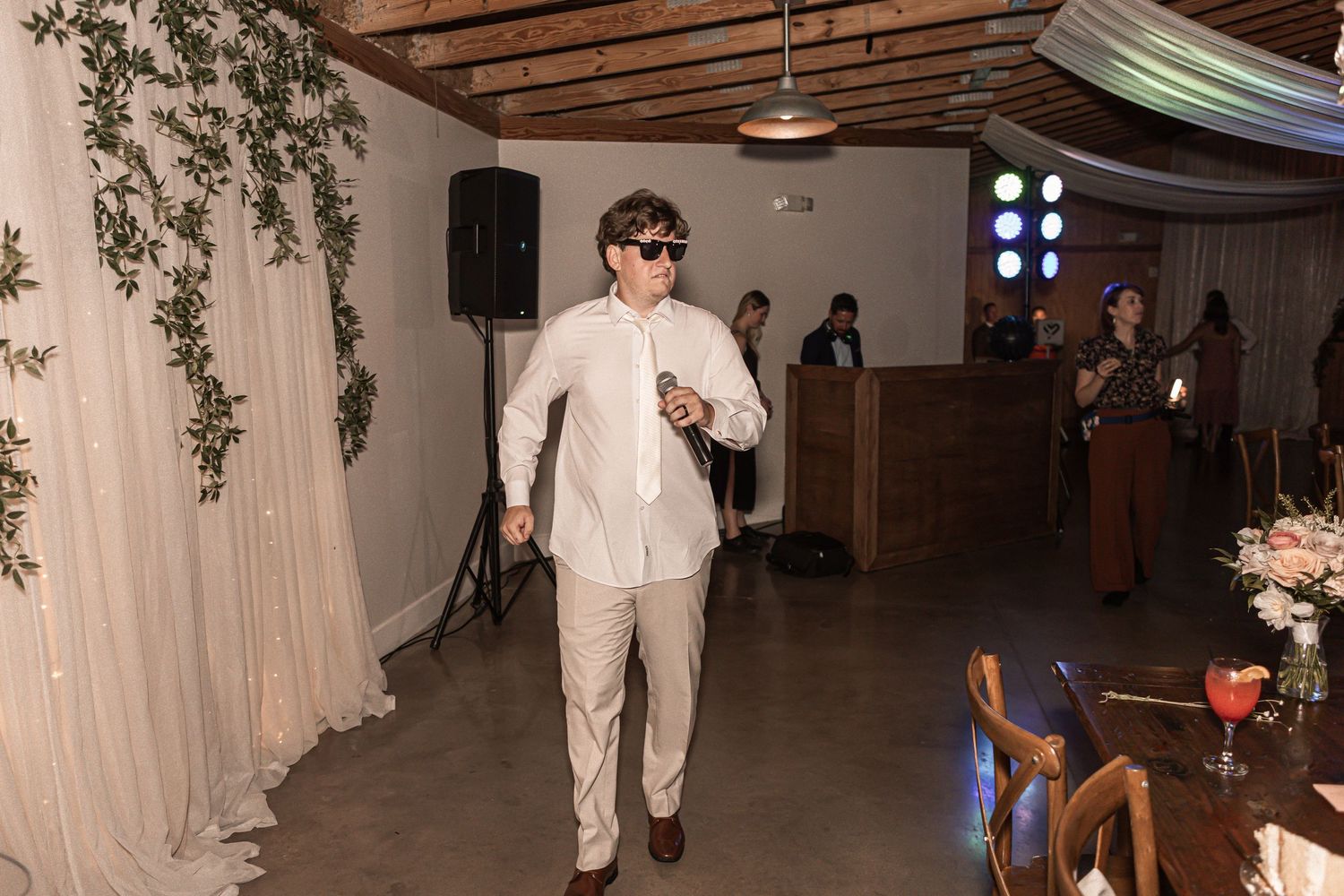 Dancing at a wedding reception with stage lights and draped fabric decor in an indoor venue.