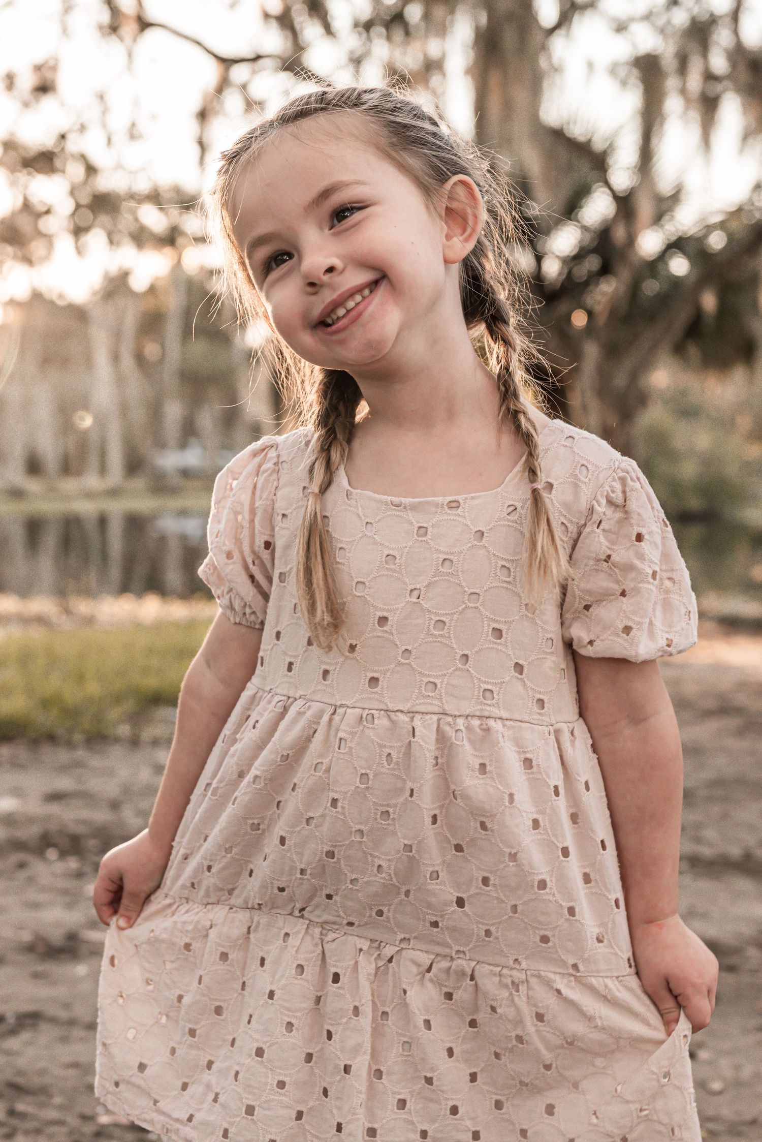 A sweet outdoor portrait featuring a cream-colored eyelet dress with puff sleeves in warm evening light.