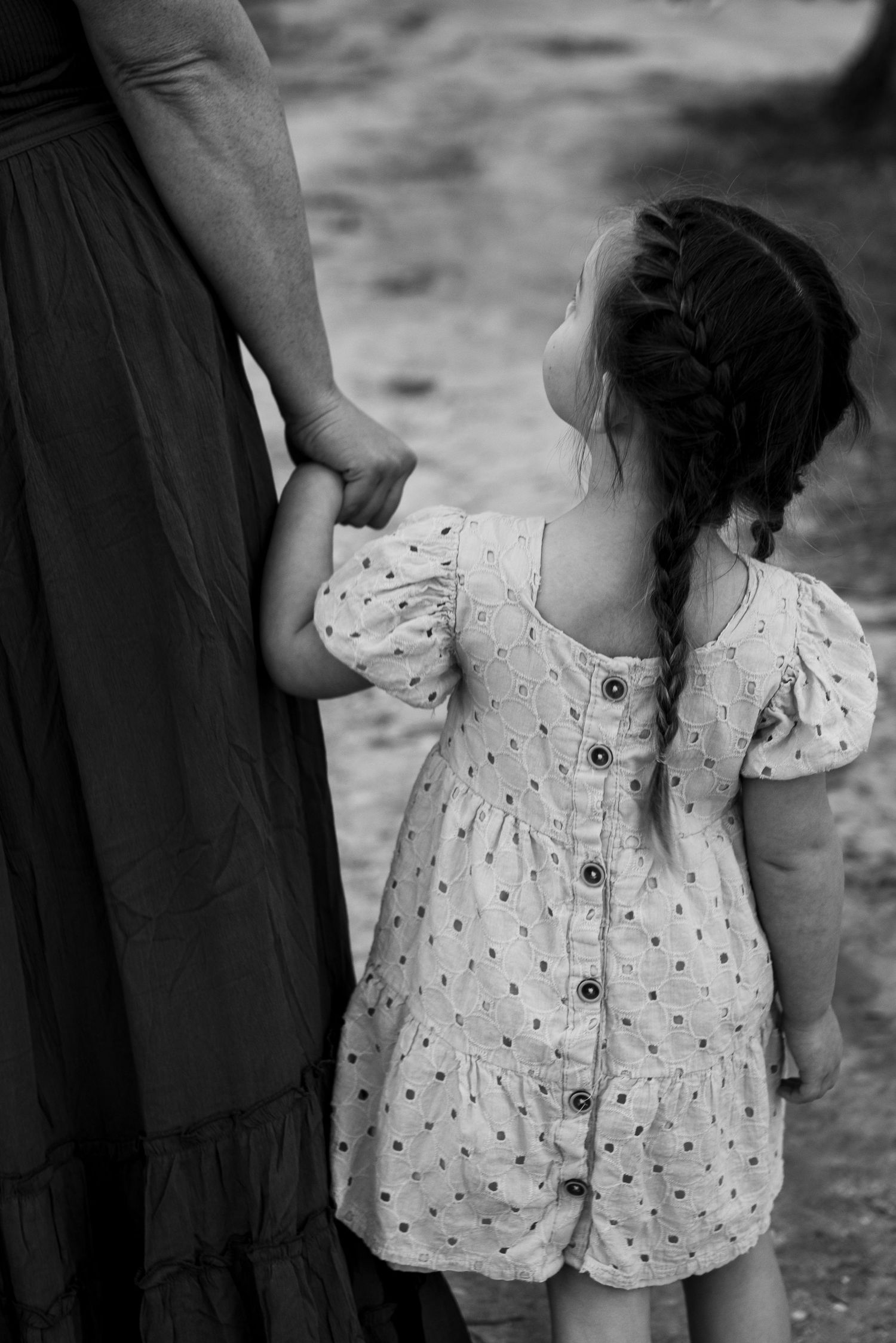 Black and white photo showing a child in a polka dot dress holding hands with a person in a long dress.