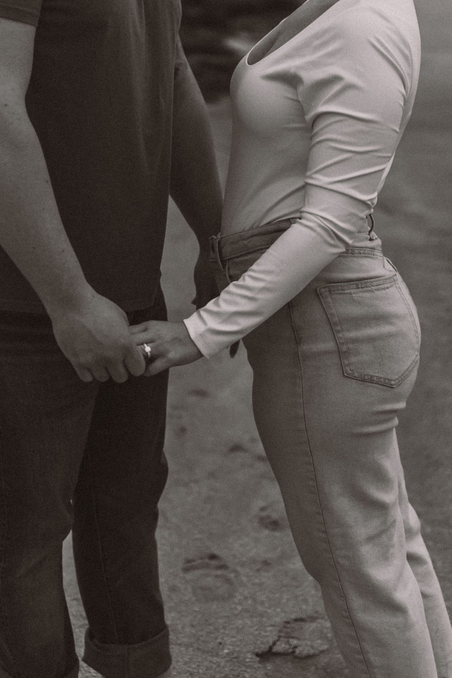 Black and white close-up of couple holding hands while standing together outdoors.