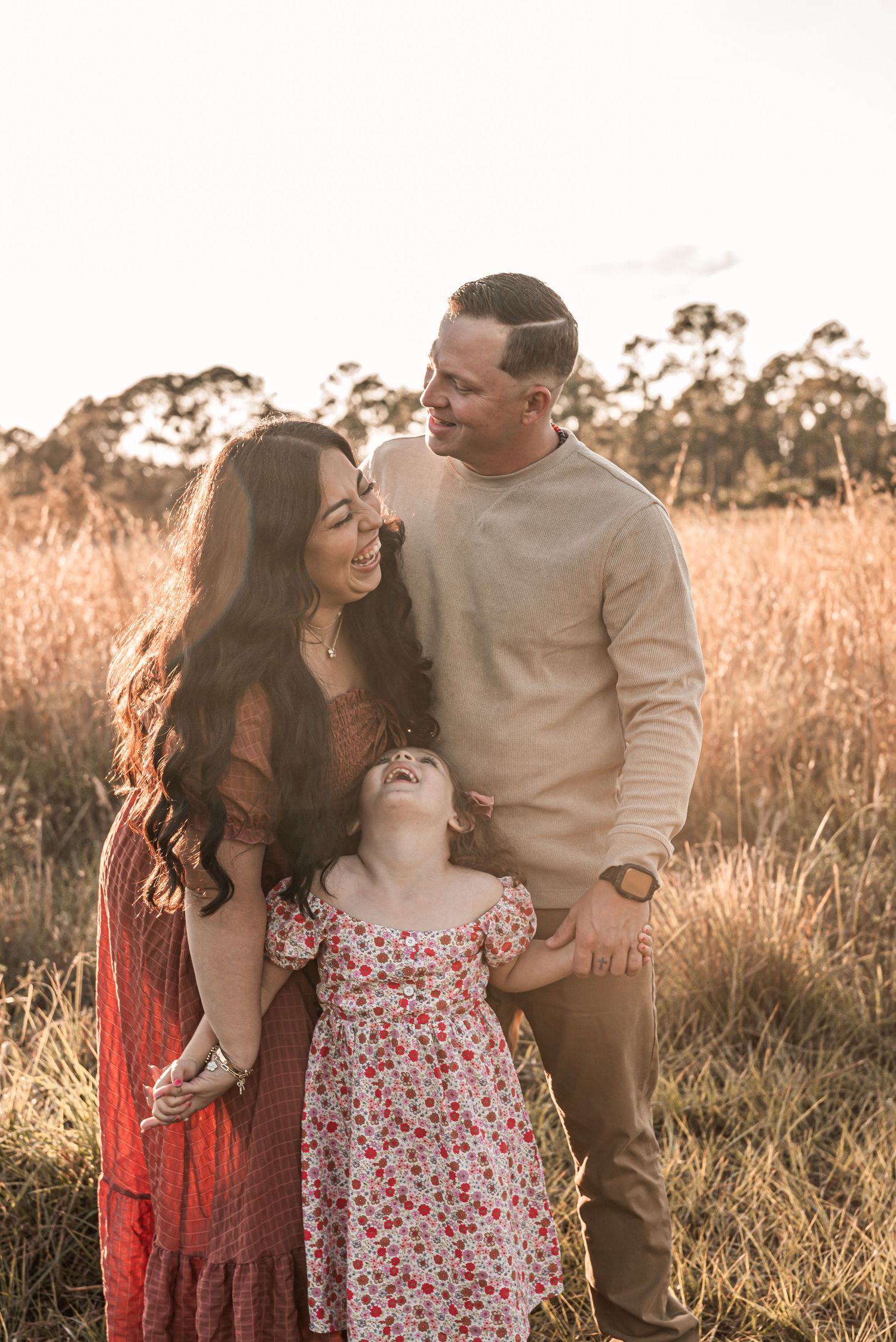 Family shares joyful moment together in golden field at sunset wearing coordinated outfits in warm earth tones.