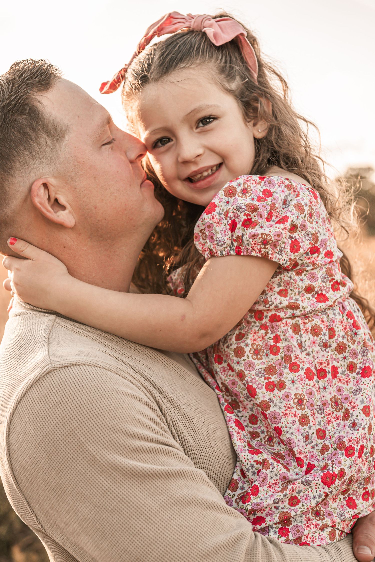 Parent and young child sharing a tender moment outdoors at sunset wearing floral dress and beige sweater.
