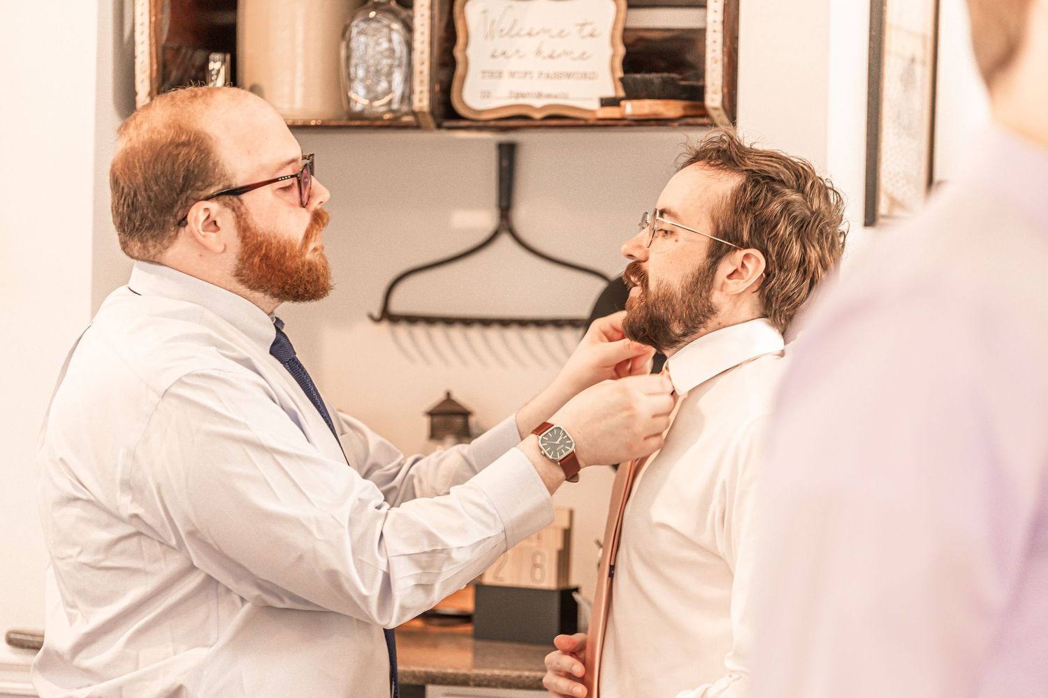 A barber gently trims a customer's beard while both men wear white button-up shirts.