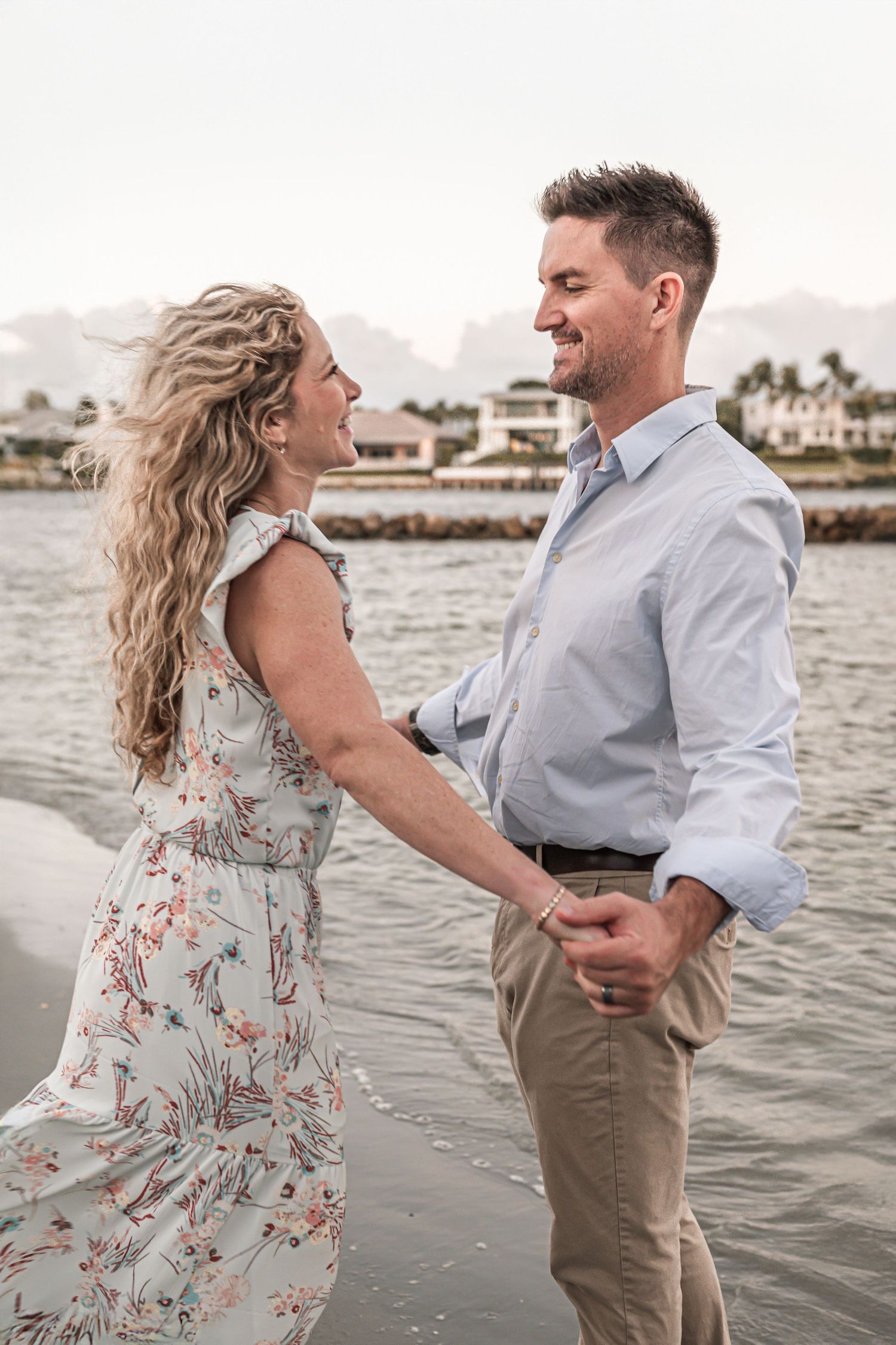A romantic couple shares an intimate moment on the beach at sunset, with palm trees and water in the background.