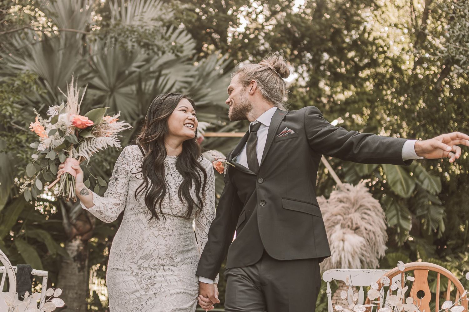 Joyful wedding couple celebrating with arms outstretched in a garden setting with a dog.