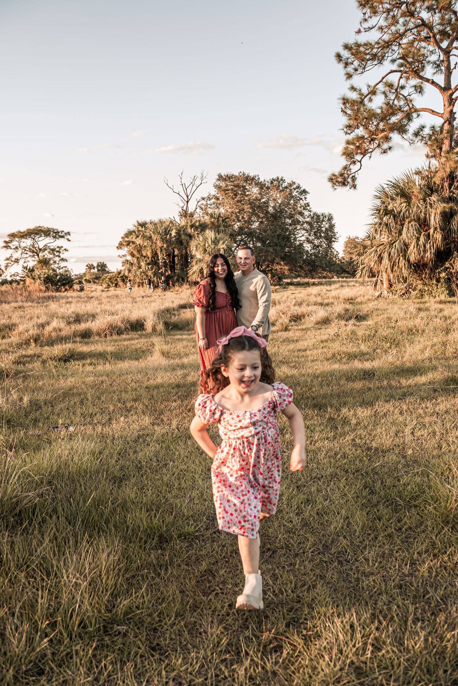 A family poses together in a sunlit grassy field with trees in the background during golden hour.