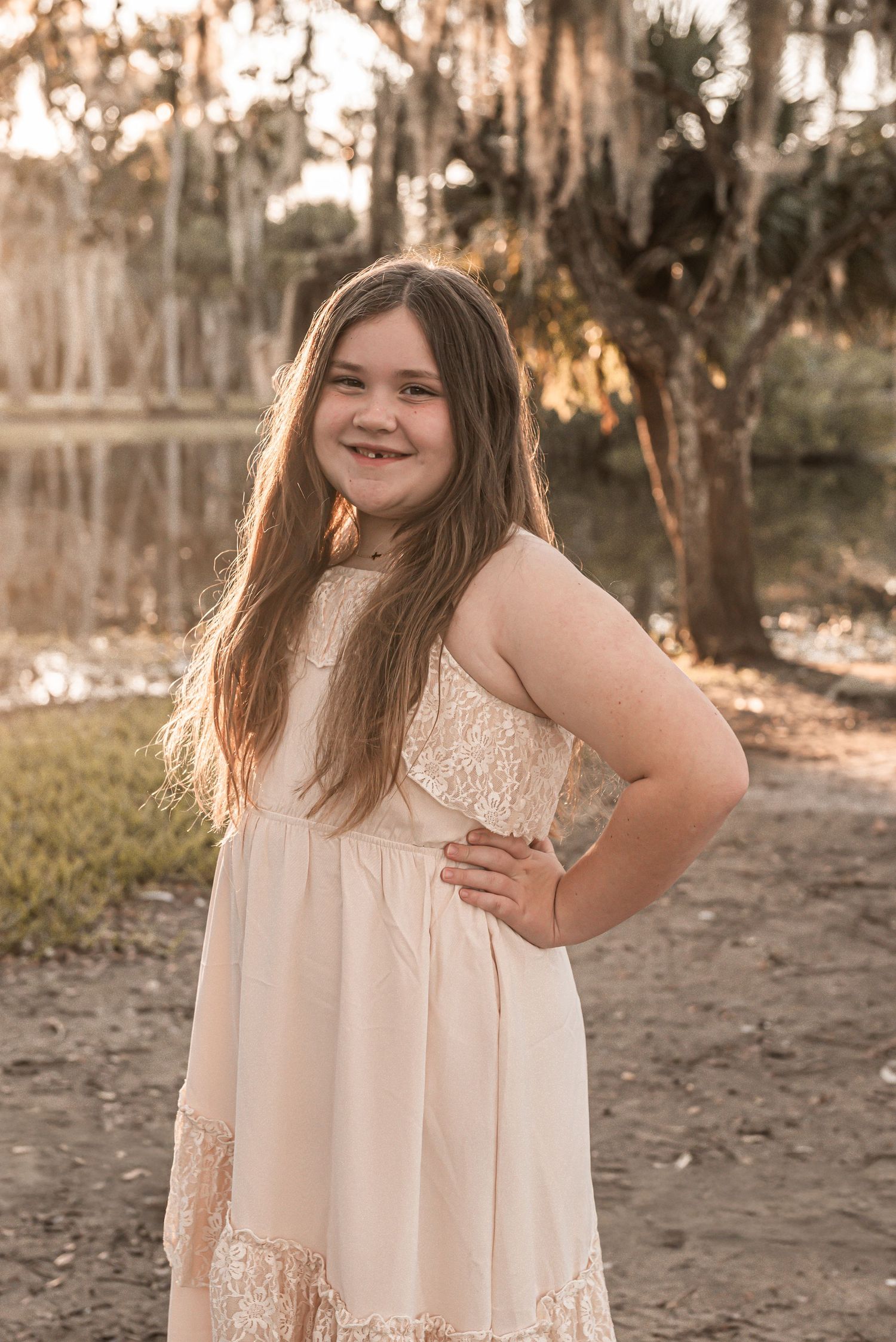 A joyful outdoor portrait in a flowing cream lace dress against a backdrop of Spanish moss and sunset lighting.