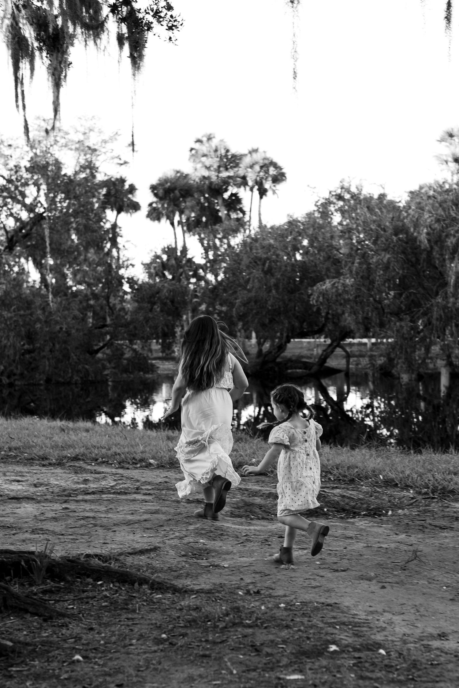 A joyful black and white vintage photo of siblings playing in a field with Spanish moss draped trees in the background.