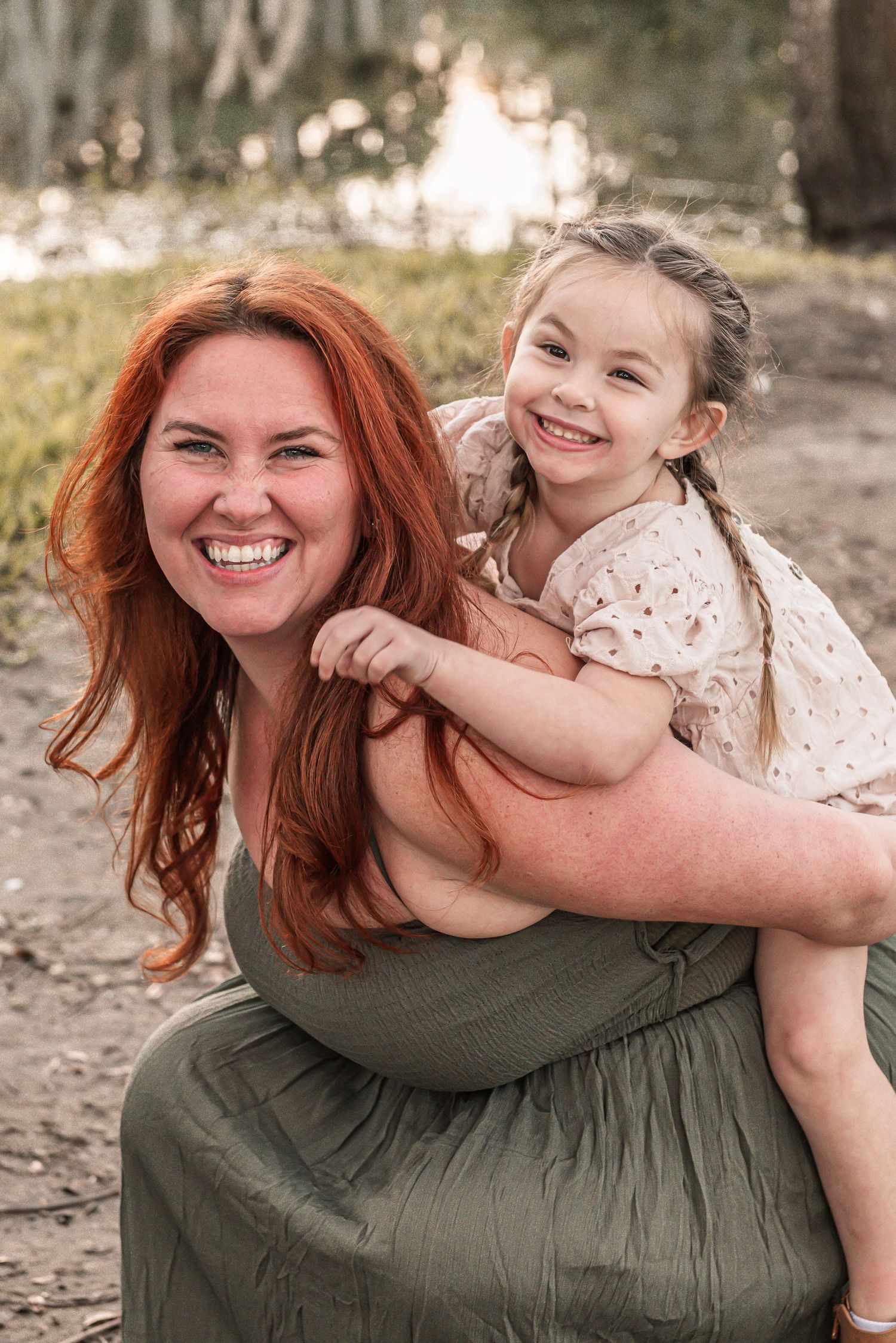 Two smiling people share a playful piggyback ride moment outdoors in warm sunset lighting.