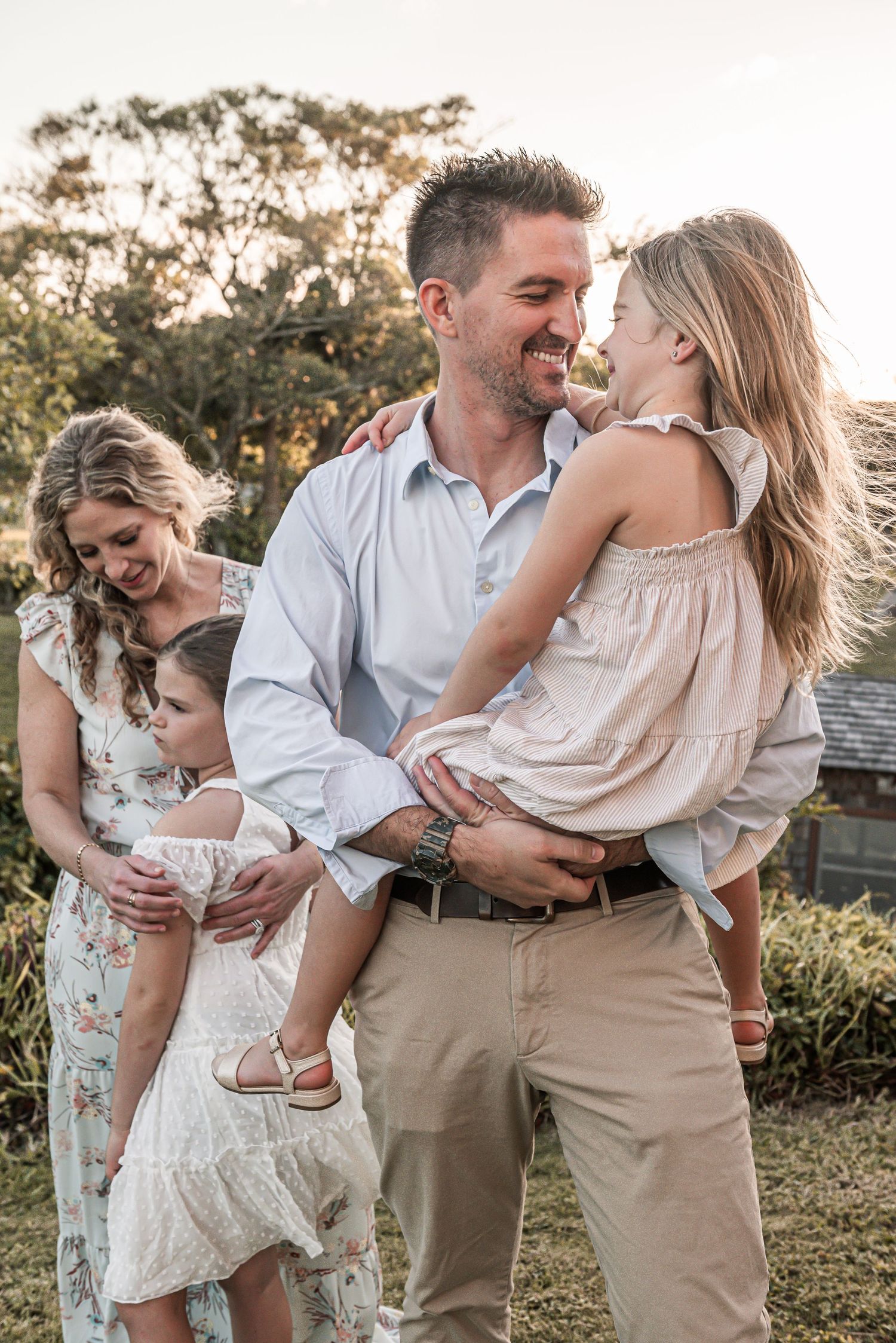 Family shares joyful moment together outdoors during golden hour sunset in a garden setting.