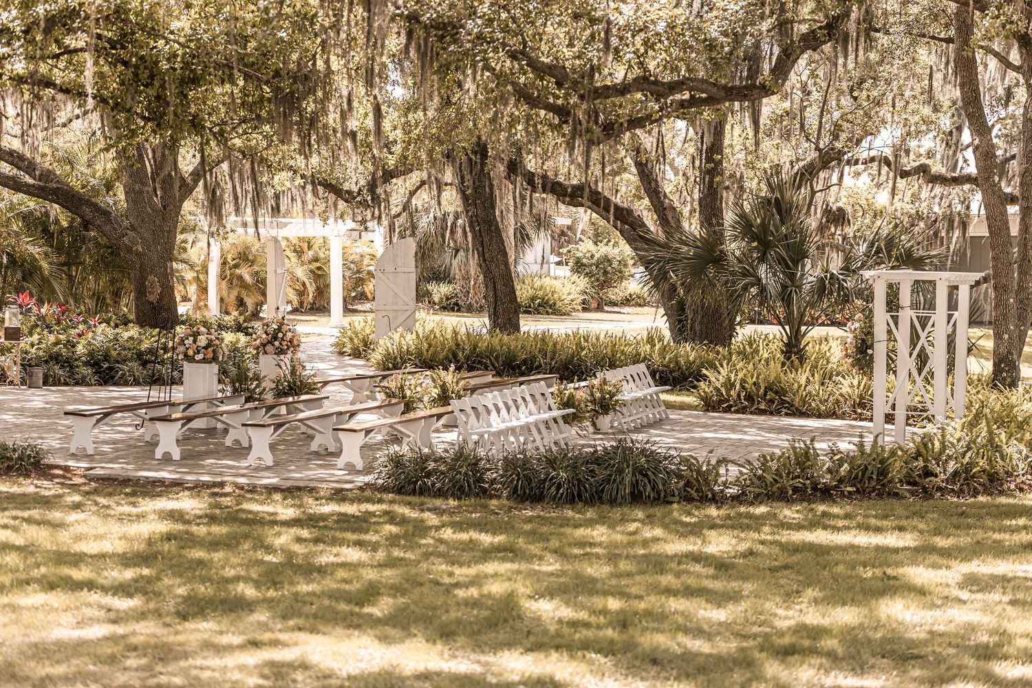 Romantic garden setting with Spanish moss draped trees, white gazebo and stone pathways in soft sunlight.