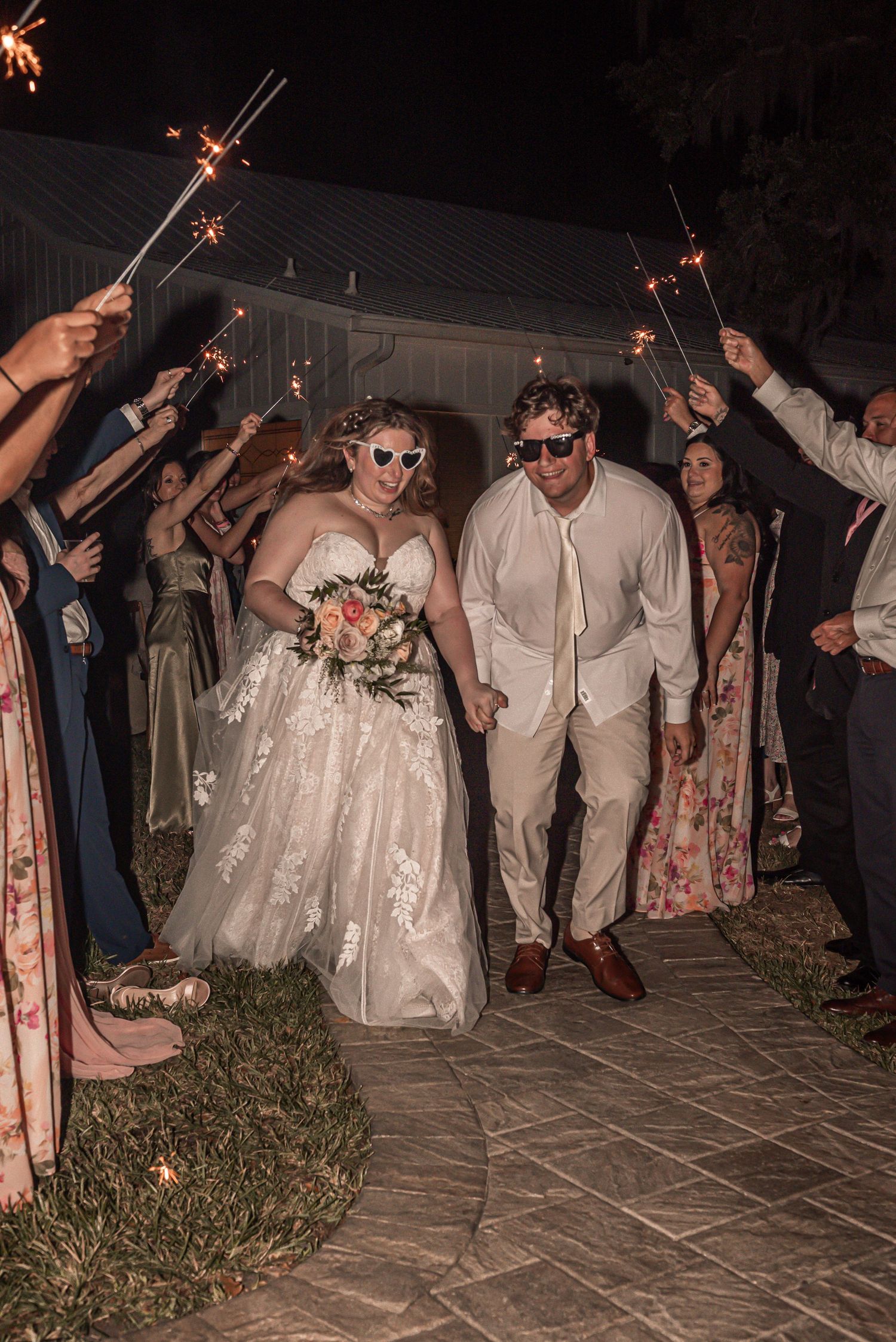 Wedding couple walking beneath a sparkler arch held by guests on a stone path during their evening reception celebration.
