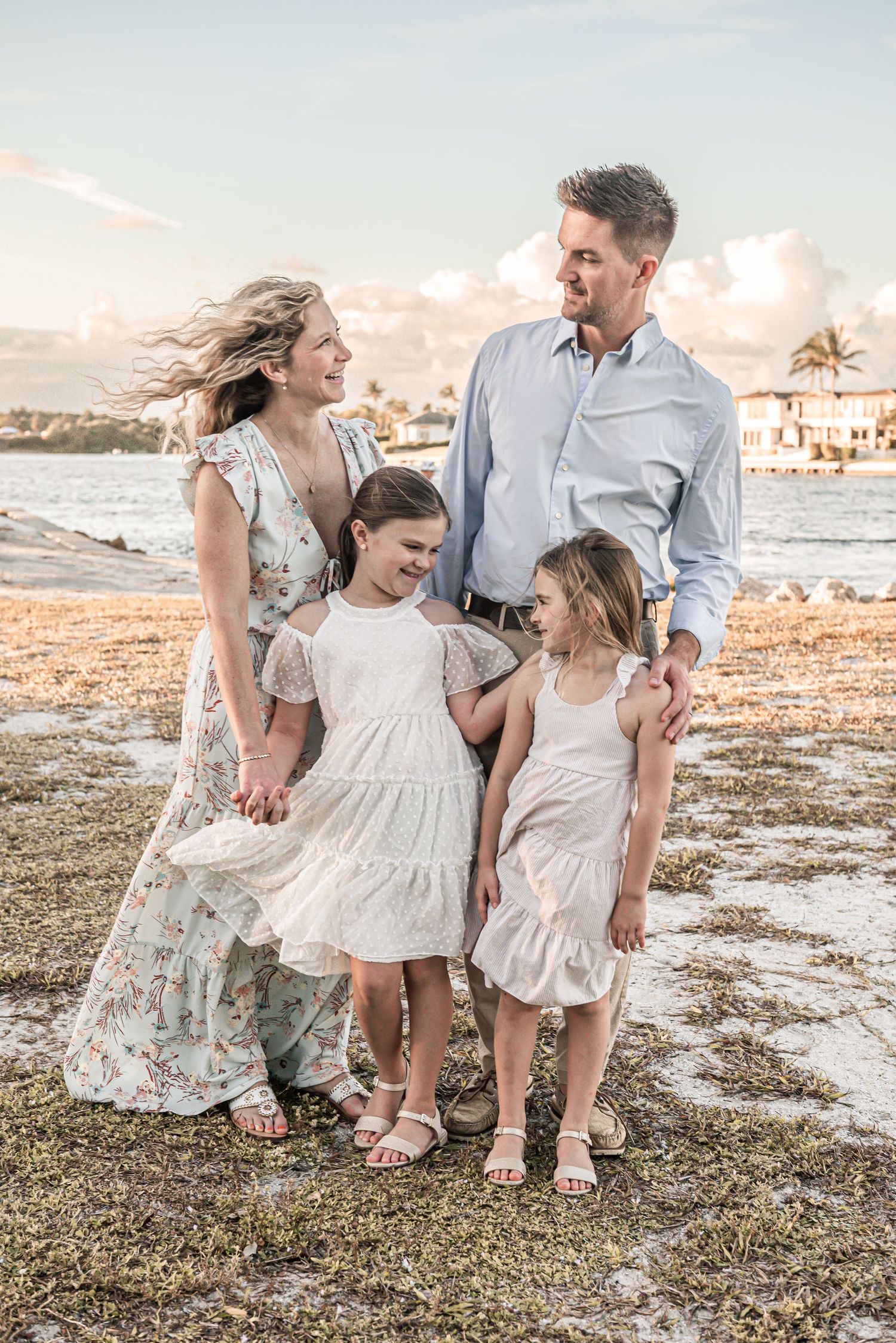 A family of four enjoys a sunset moment together on a tropical beach wearing coordinating white and floral outfits.