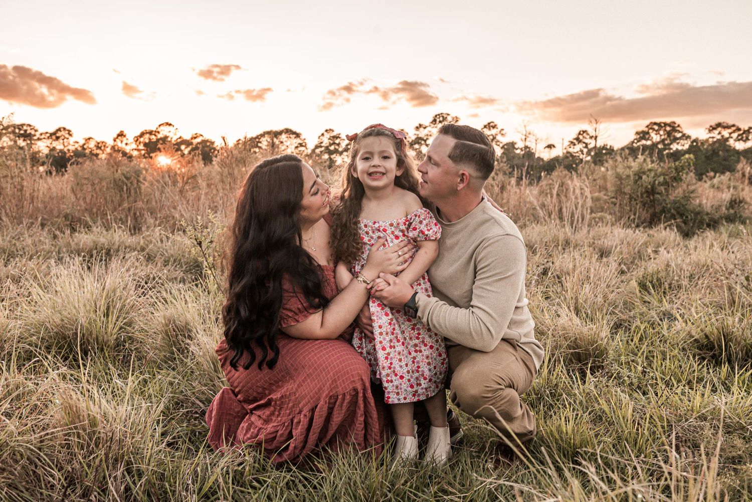 A family enjoying a tender moment together in a golden field at sunset.