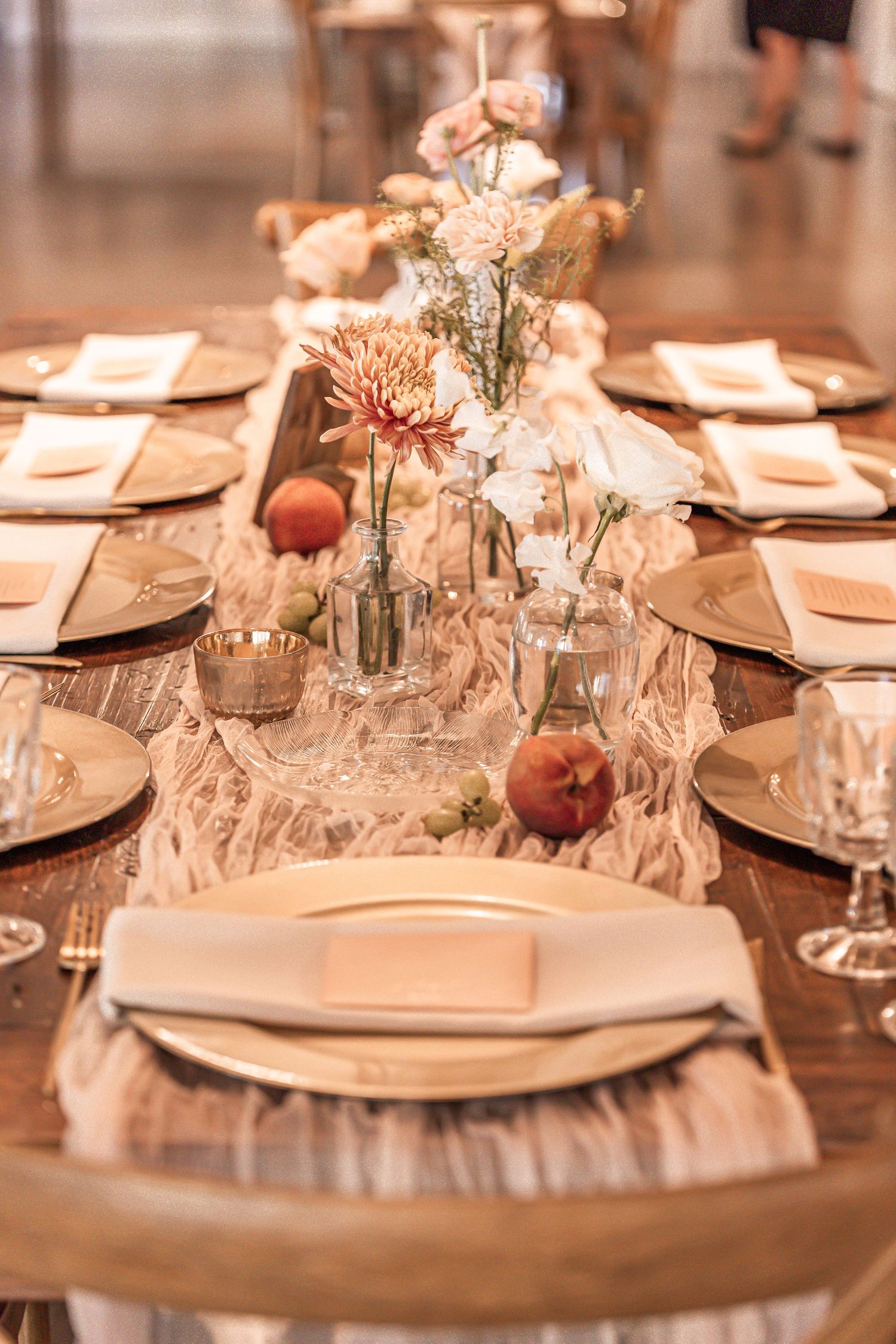 An elegant wedding table setting with peach and cream decor, fresh florals in glass vases, and delicate place settings.