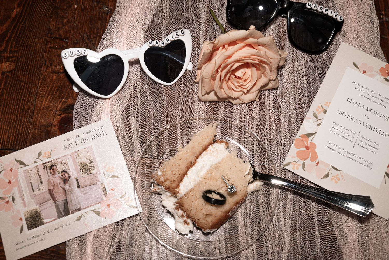 Heart-shaped sunglasses, pink rose, and wedding invitations arranged on a rustic wooden surface with a vintage photograph.
